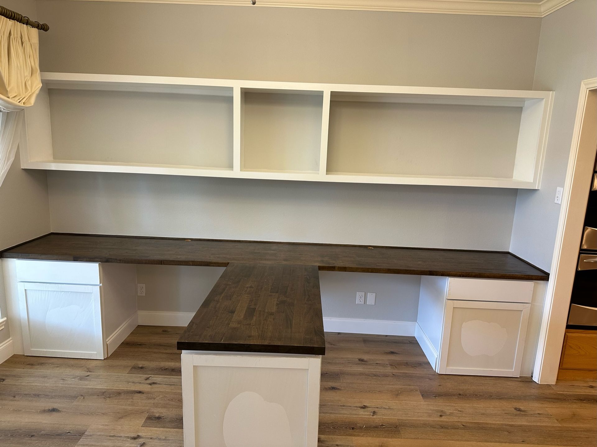 Built-in office desk with dark wood countertop, white cabinets, and shelves against a light gray wall.