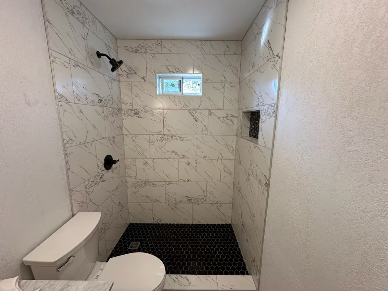 Bathroom with white marble tile shower, black pebble floor, and toilet.