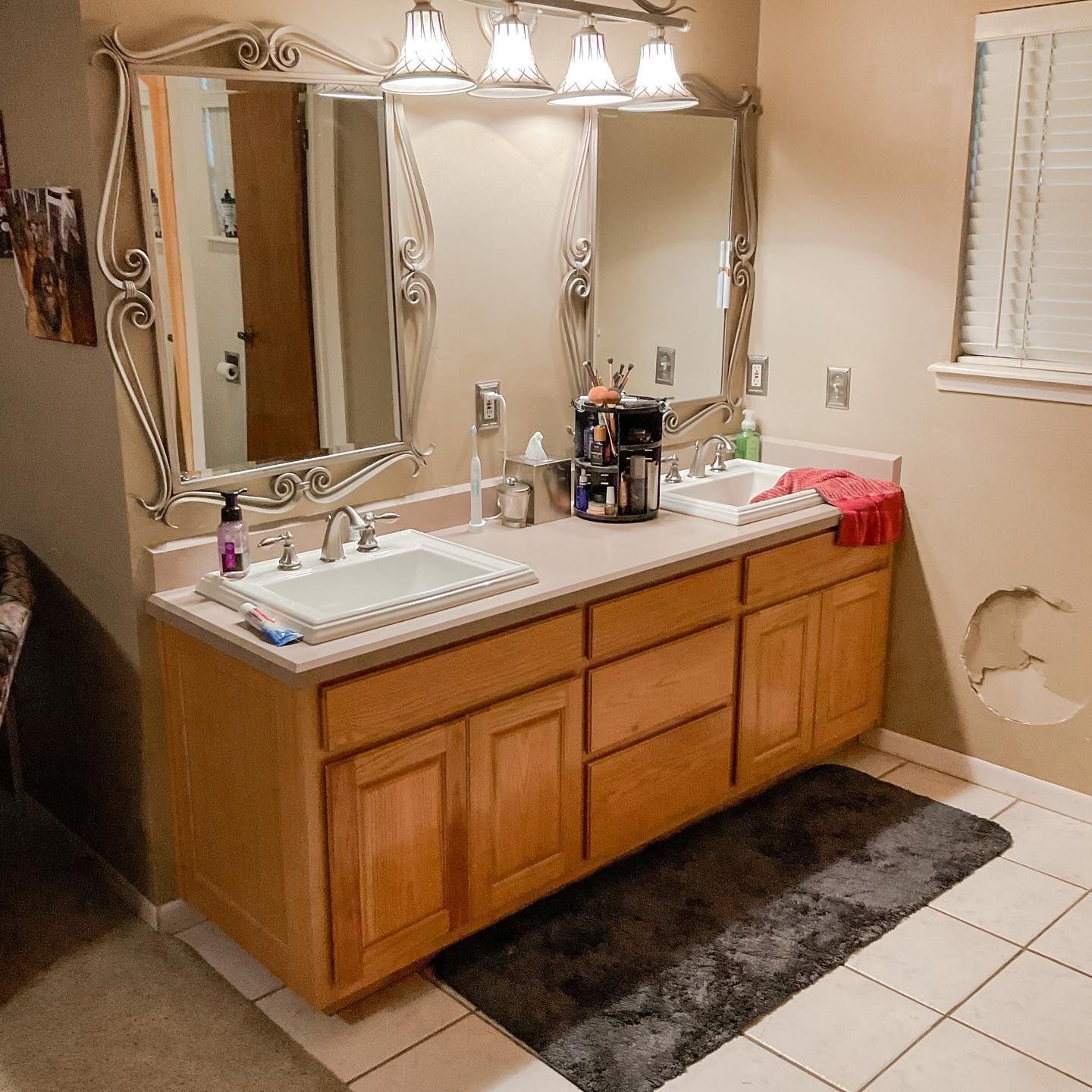 Bathroom with double sinks, mirrors, wooden cabinets, and a gray rug.