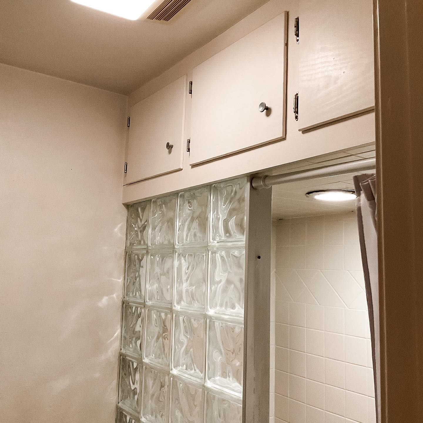 Bathroom with glass block shower wall, white cabinets, and a shower curtain.