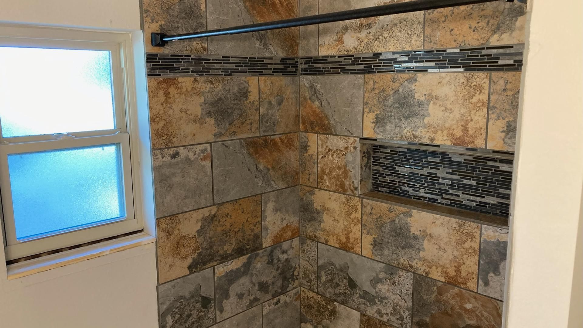 Shower with multi-colored stone tiles, a glass mosaic accent, and a window.