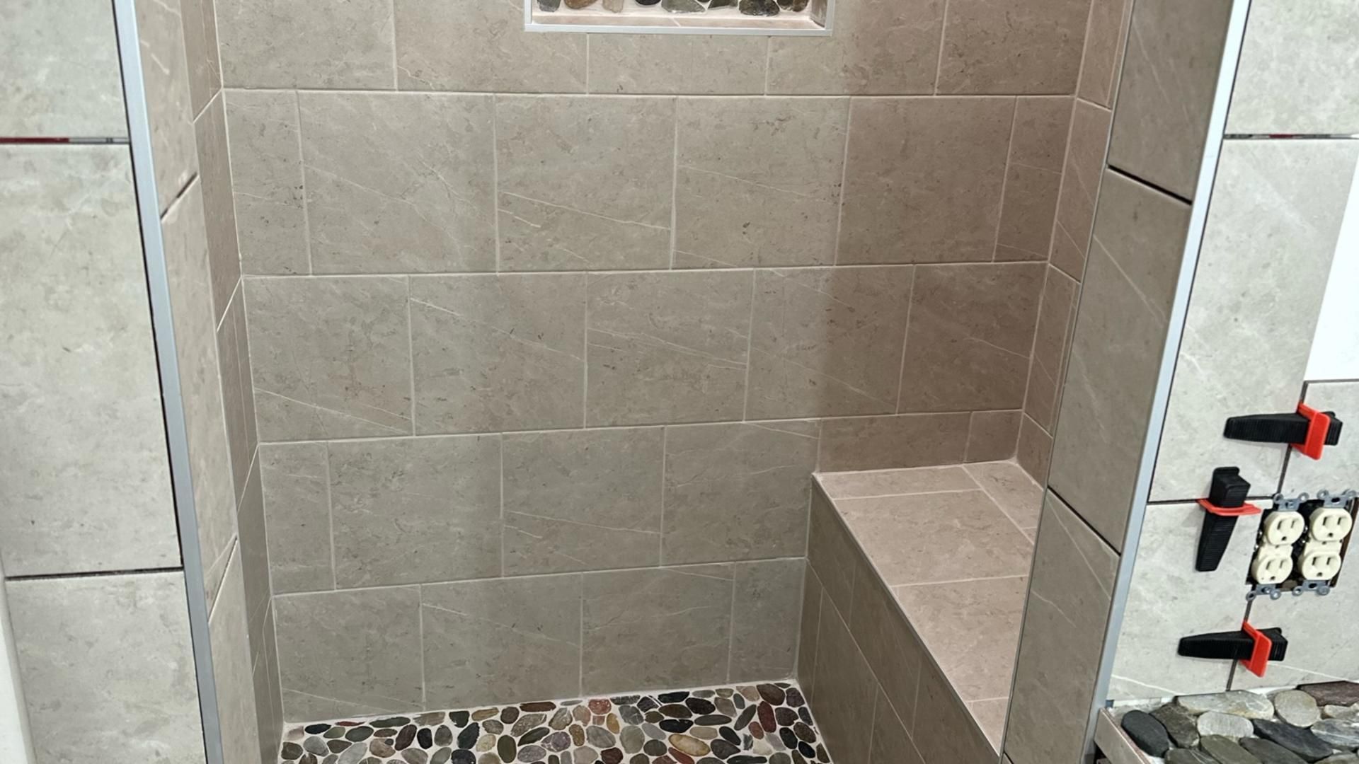Shower stall tiled in gray with a pebble floor and a built-in bench.