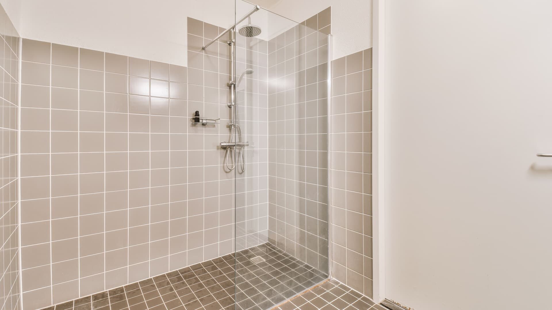 Gray tiled shower with glass door and shower fixtures.