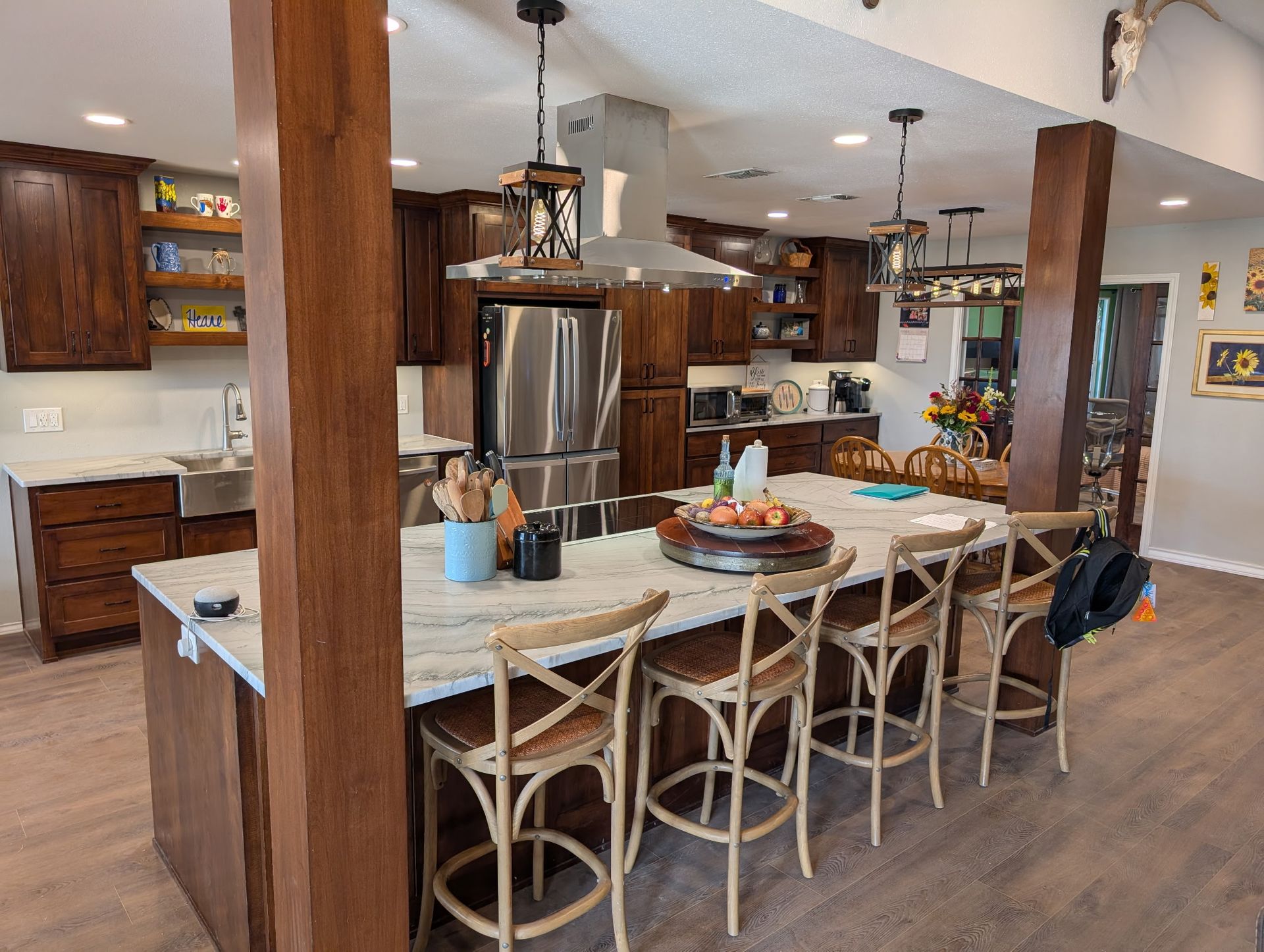 Kitchen with brown cabinets, island with stools, stainless steel appliances, and wooden support beams.
