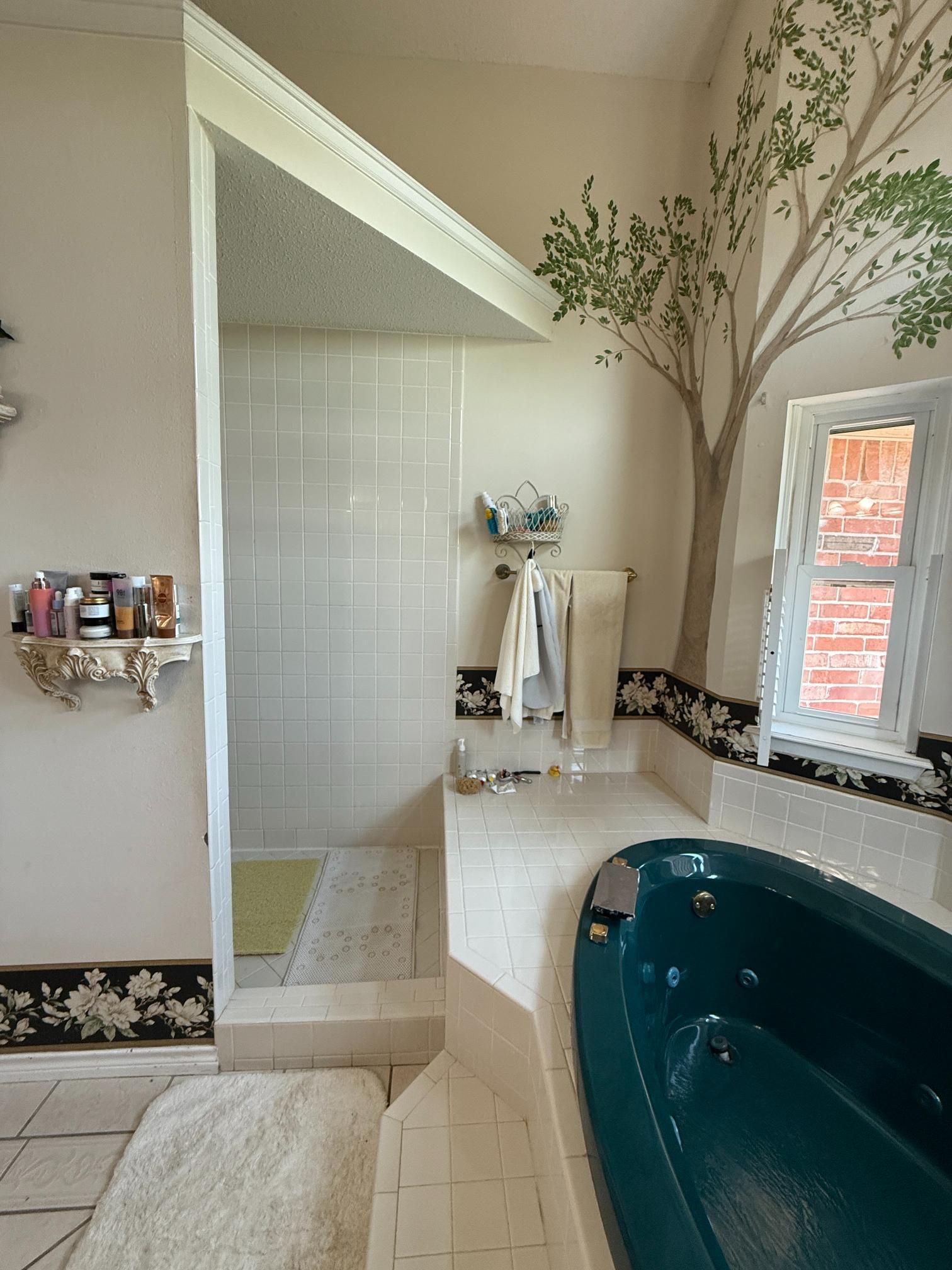 Bathroom with teal tub, white tile shower, and tree mural.