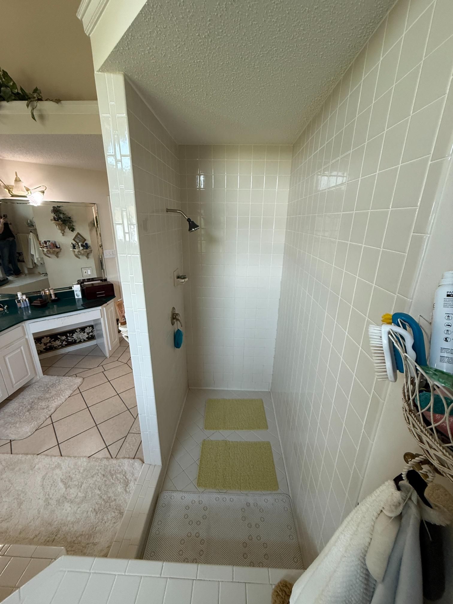 Walk-in shower with white tile walls and floor, two green bathmats. White towels hang outside shower.