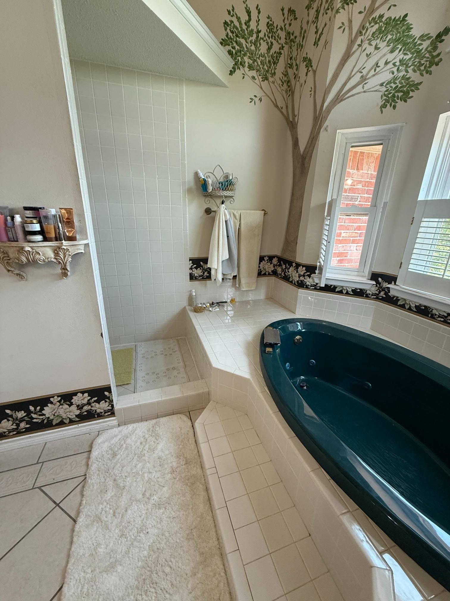 Bathroom with teal tub, shower, tree mural, and white tile.