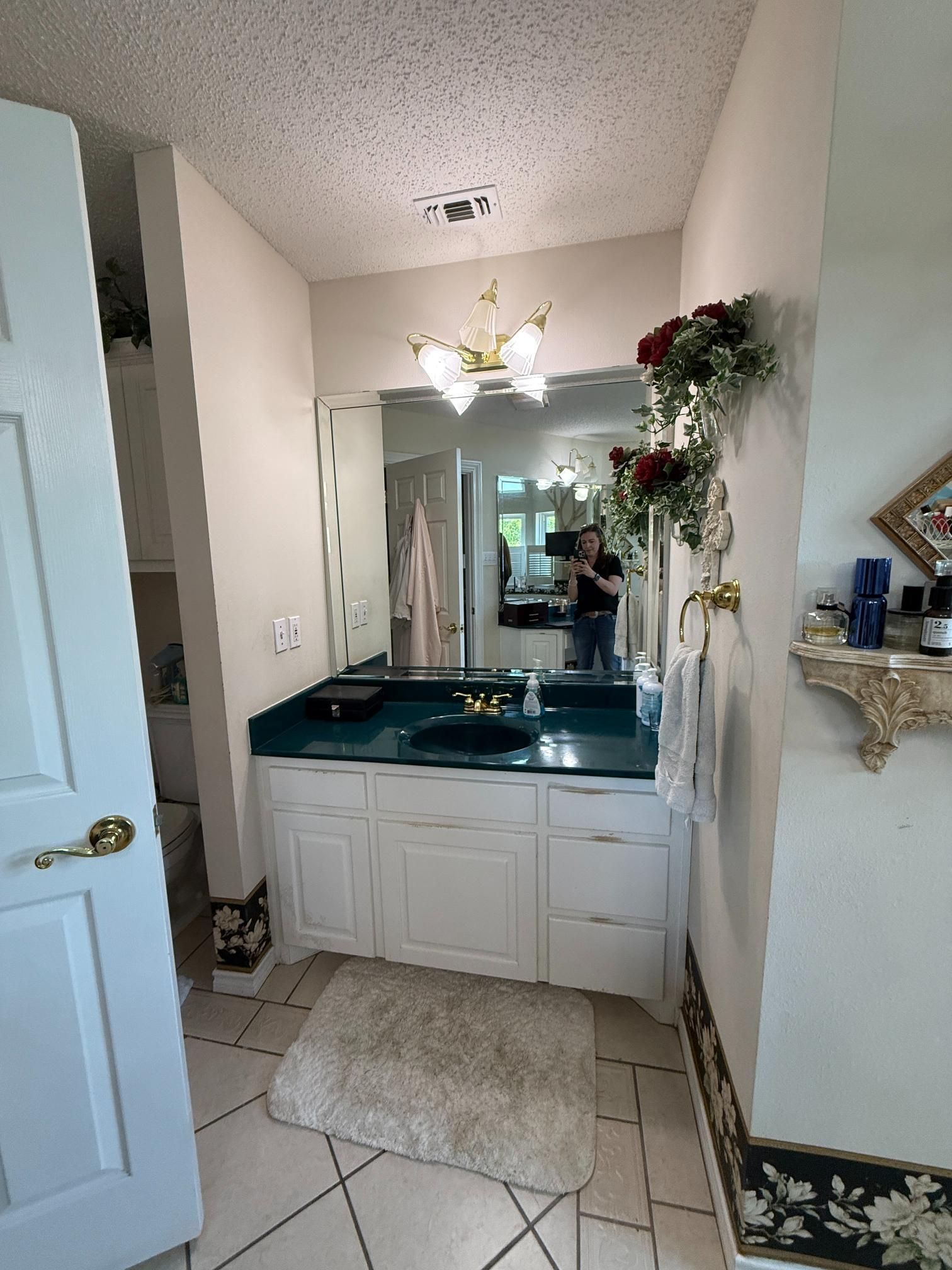 Bathroom with white cabinets, green countertop, large mirror, and floral accents.