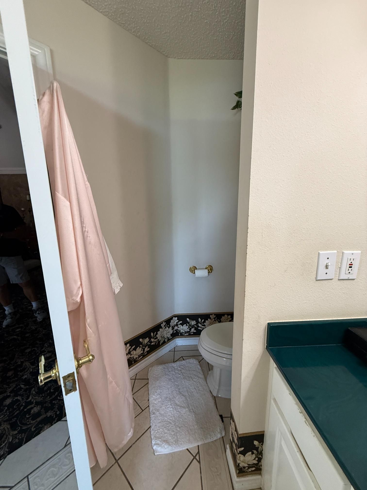 A small bathroom with a toilet, shower, and a bathrobe hanging on the door.