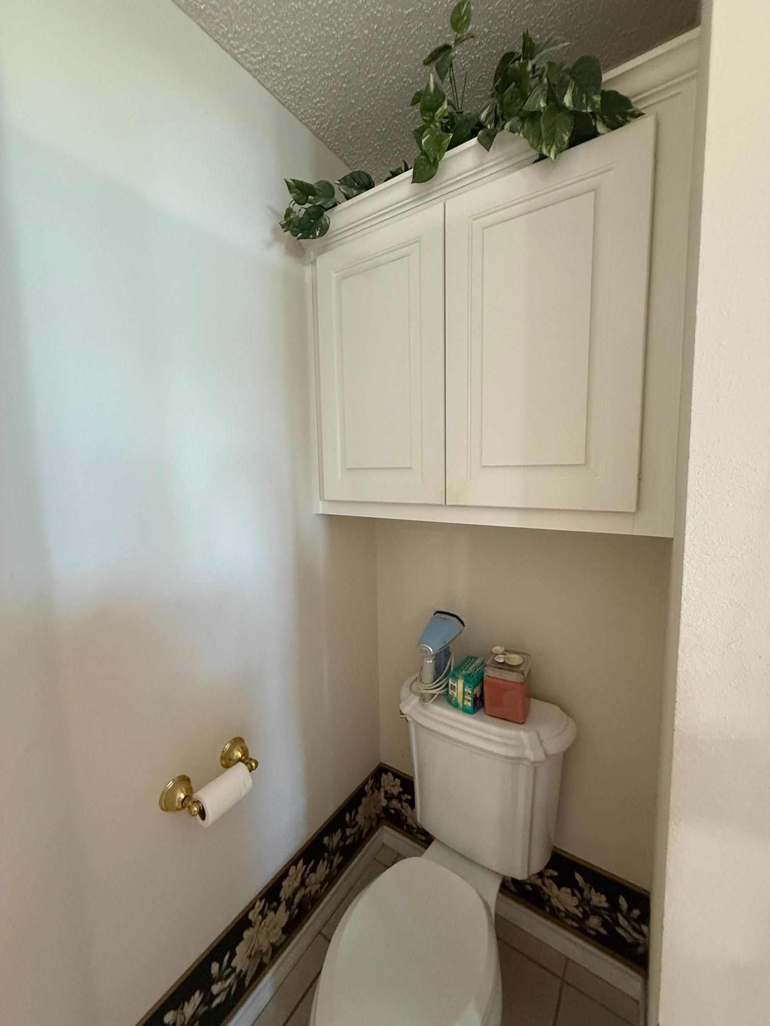 A small bathroom with a toilet and storage cabinet above. Decorative border along the base.