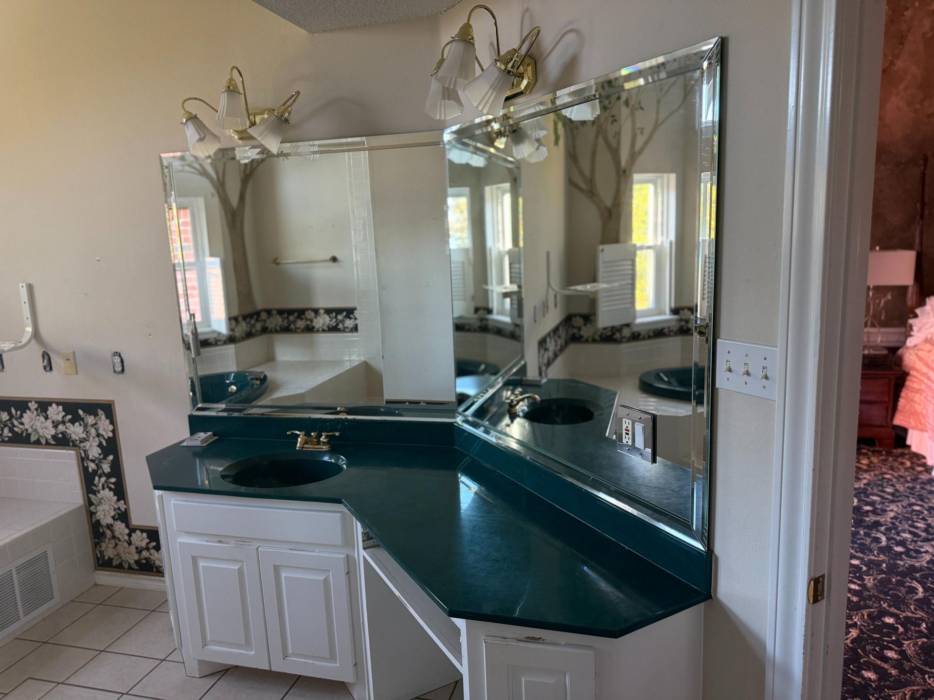 Bathroom with dual sinks, mirrors, and white cabinets. Green countertop.