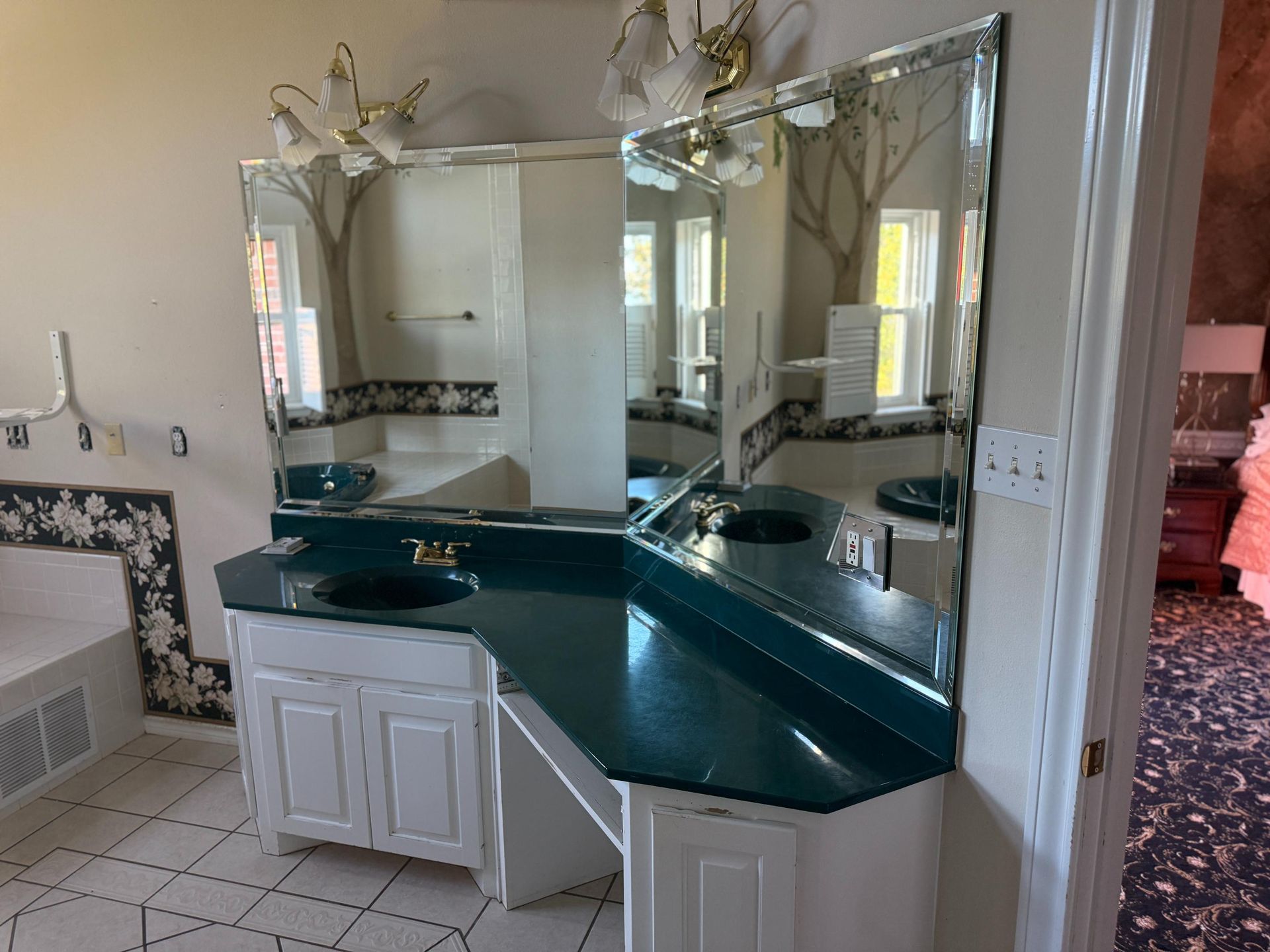 Bathroom with a double vanity. White cabinets, teal countertop, framed mirrors, and floral details.
