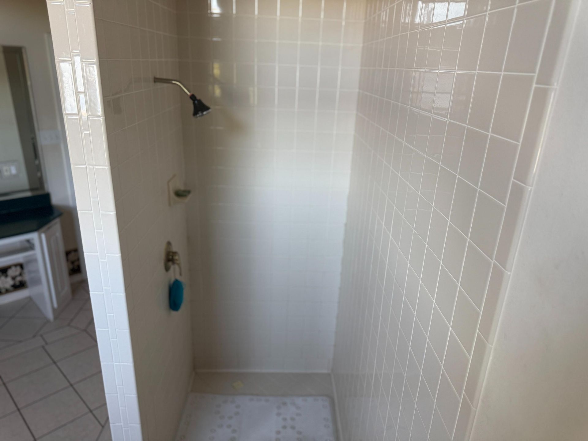 A beige tiled shower stall with a showerhead and soap holder. A blue washcloth hangs on the wall.