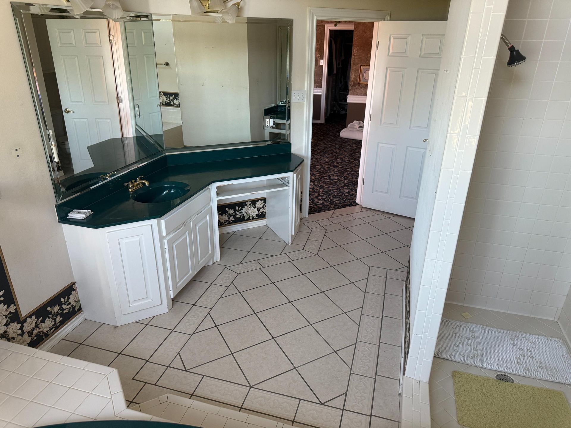 Bathroom with white vanity, dark green countertop, and tiled floor. Open door to bedroom.