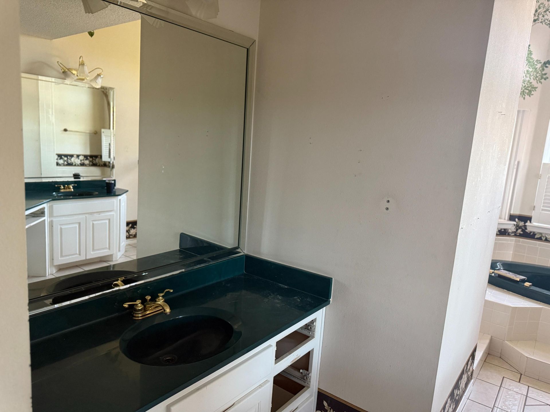 Bathroom with a dark green countertop, black sink, and white cabinets. A large mirror reflects another counter.