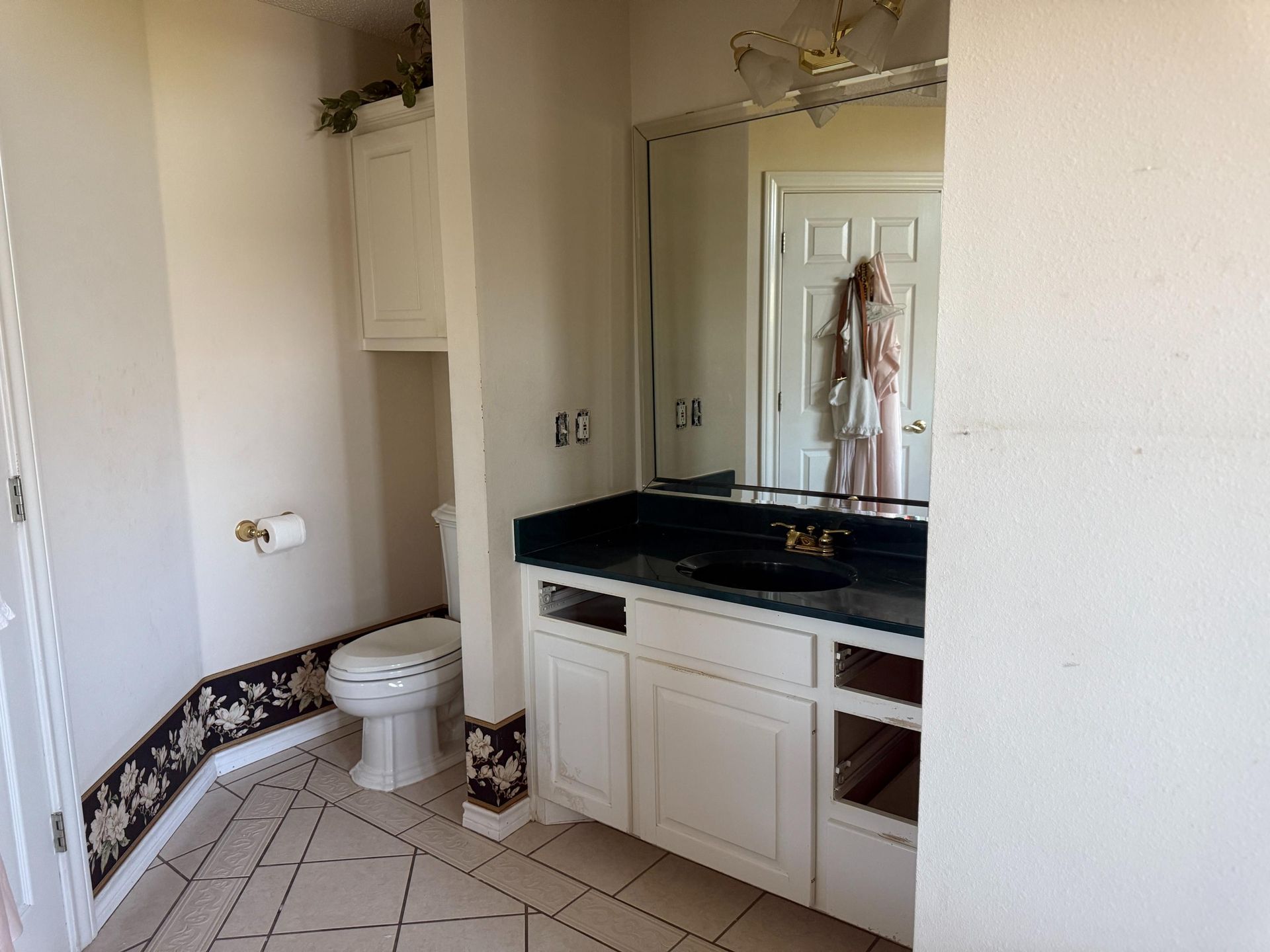 Bathroom with white cabinets, dark countertop, toilet, mirror, and partially visible door.