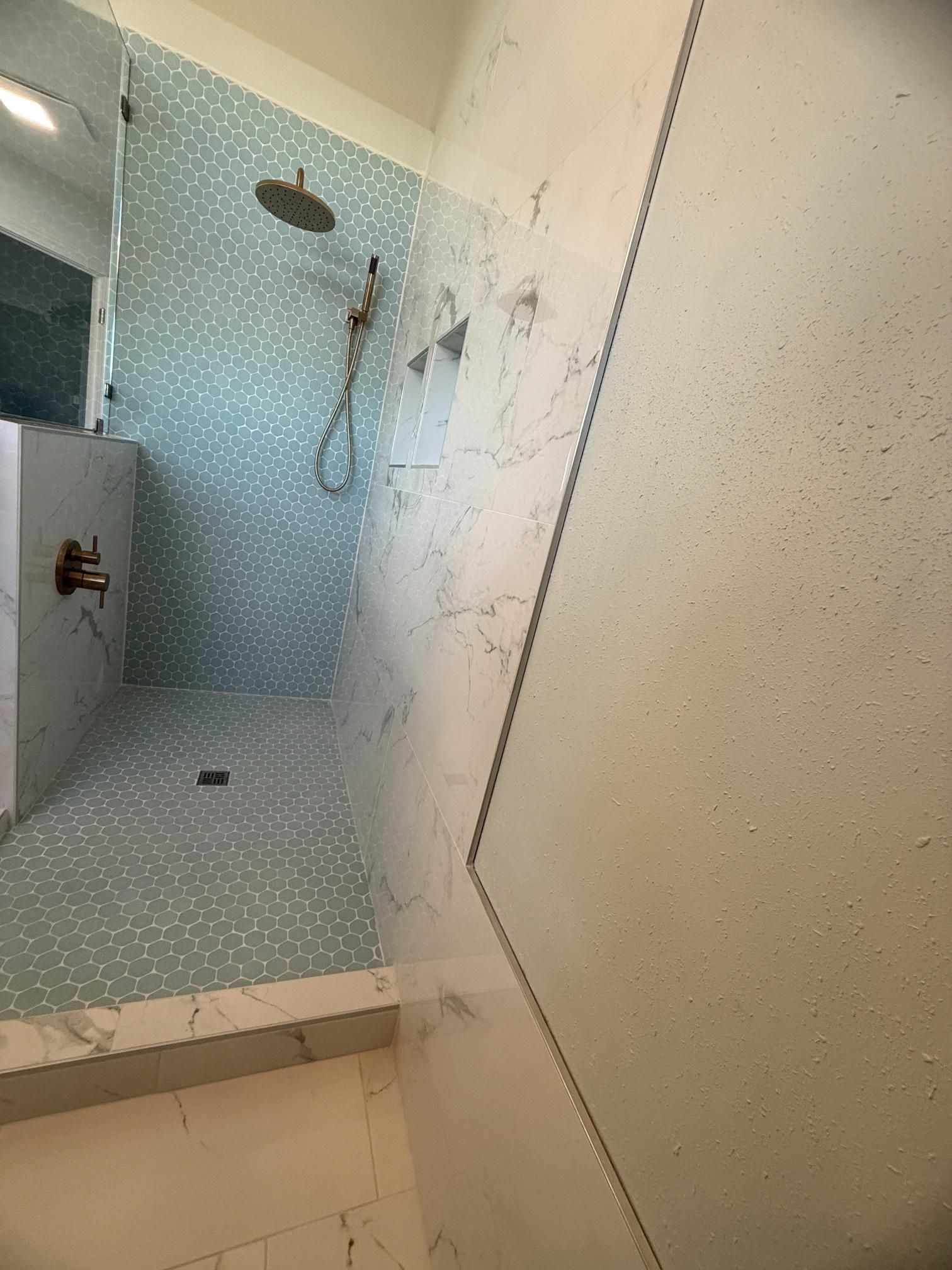Blue tiled shower with glass door and bronze fixtures.