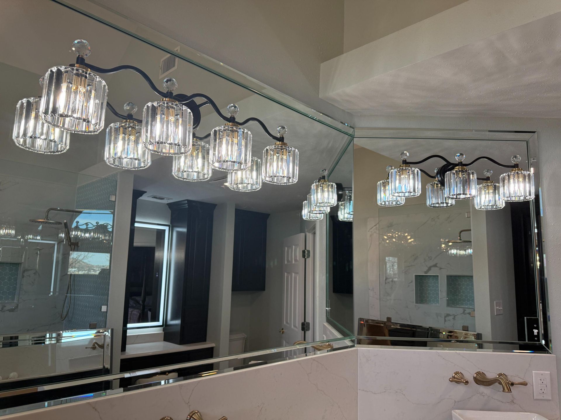 Bathroom with large mirror, crystal chandelier, white marble countertop.