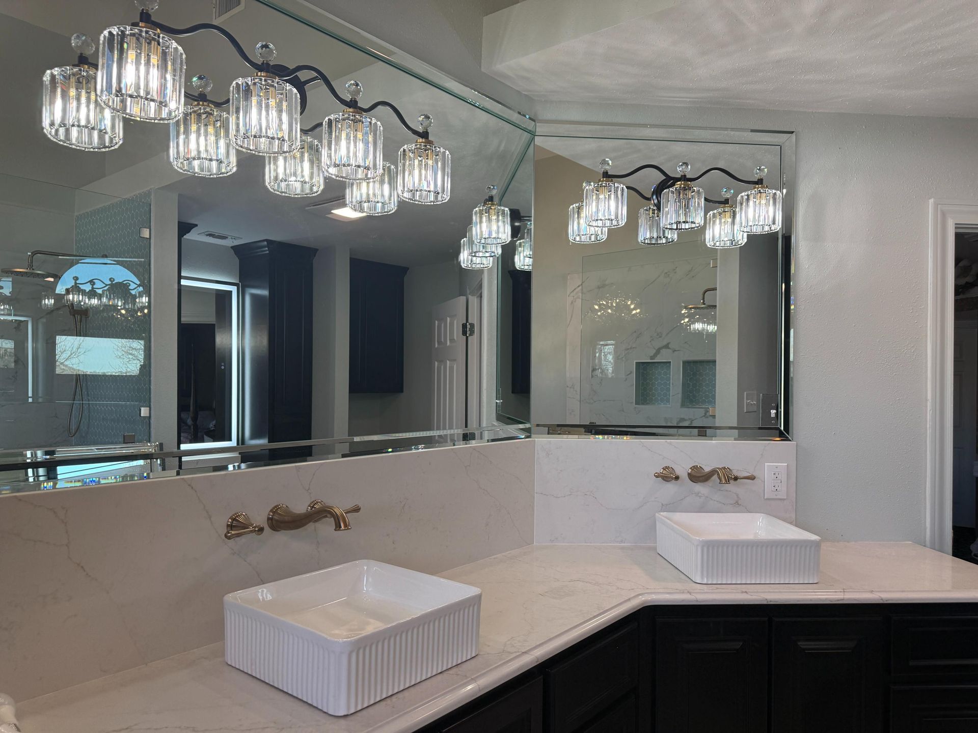 Bathroom with two sinks, large mirrors, decorative lighting, and gold fixtures on a white countertop.