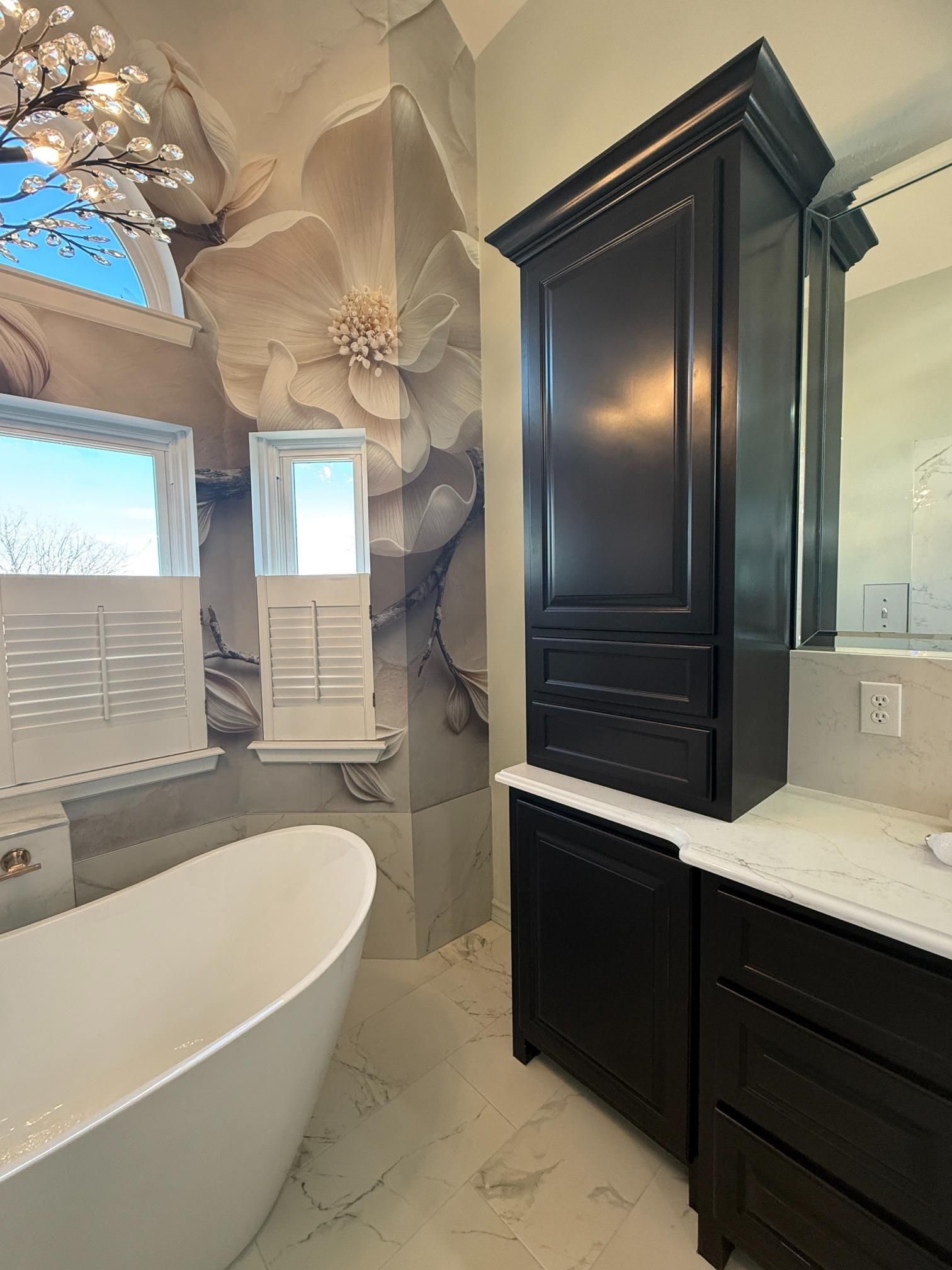 Bathroom with a white tub, dark cabinets, floral mural, and window with shutters.