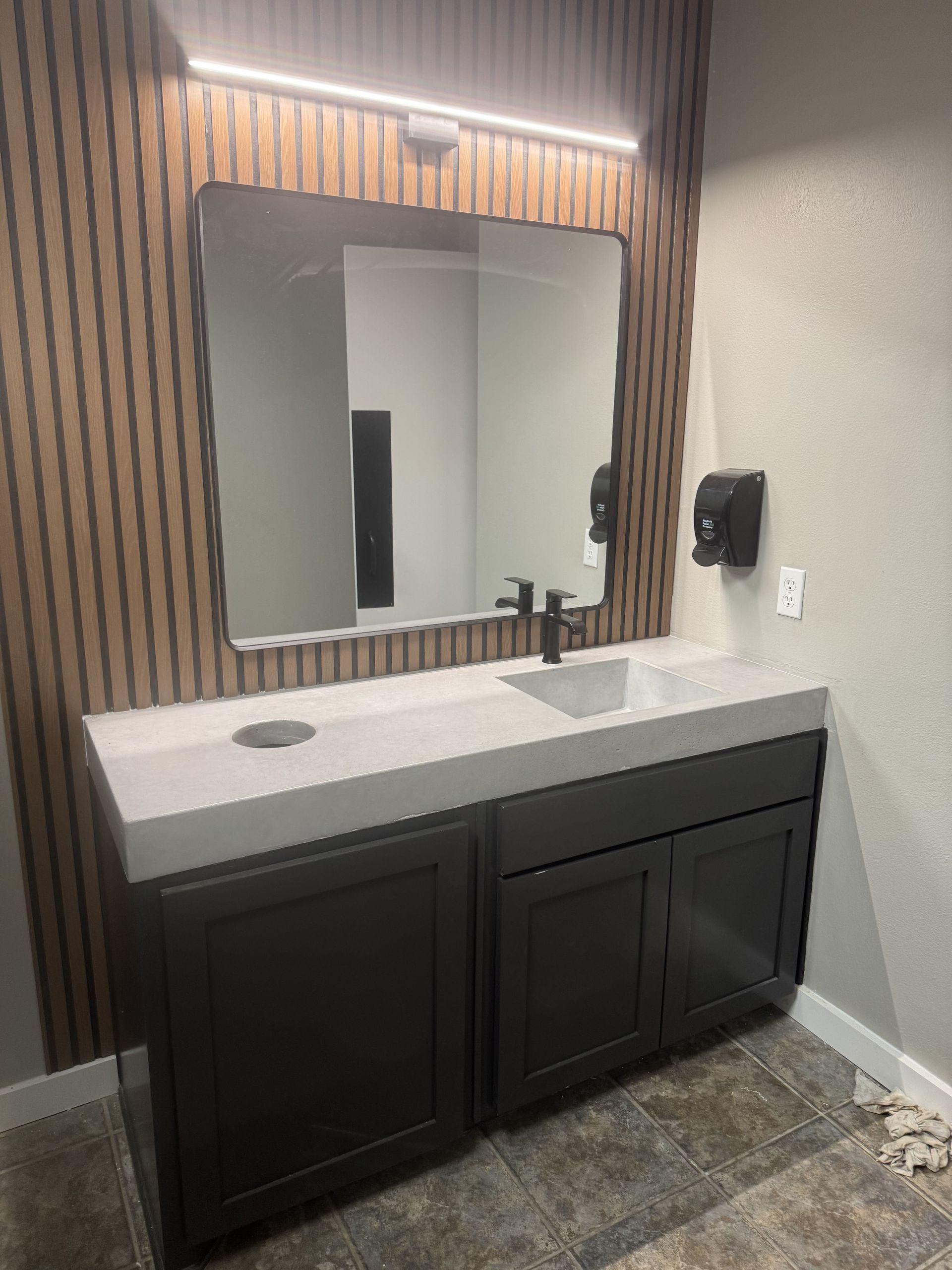 Bathroom vanity with a gray countertop, dark cabinets, a mirror, and a wood-slat accent wall.