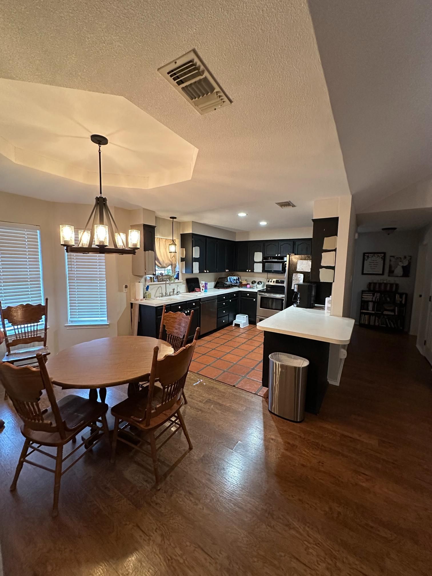 Dining room with round wooden table and chairs, leads to a kitchen with dark cabinets, stainless steel appliances, and an island.