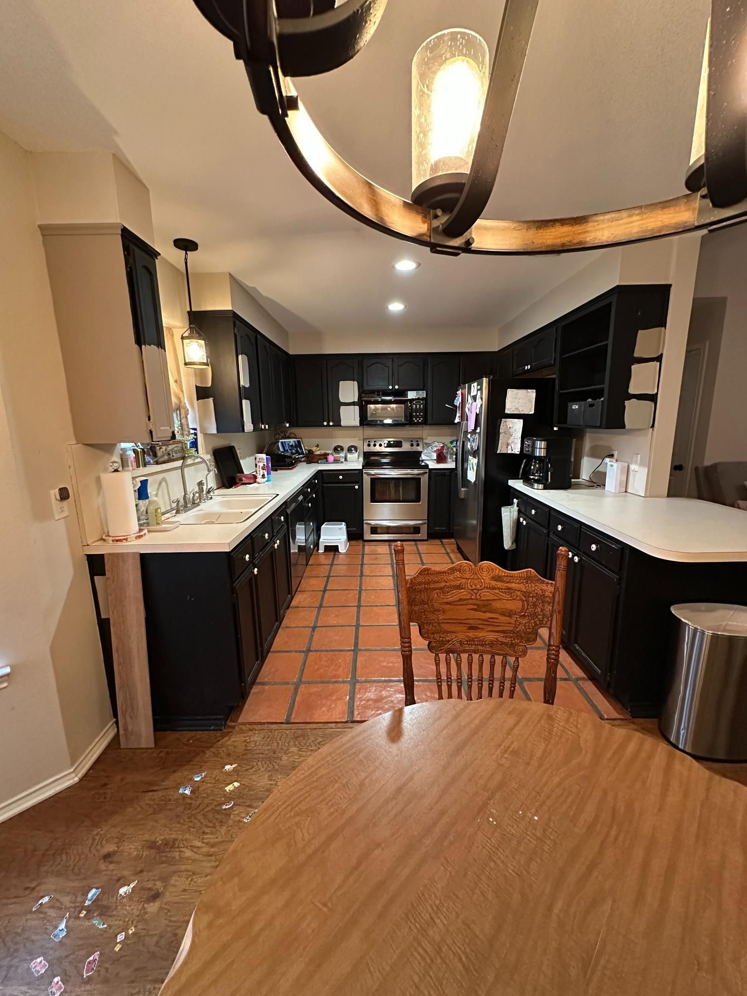 Kitchen with dark cabinets, stainless steel appliances, and terracotta tile floors. A dining table is in the foreground.
