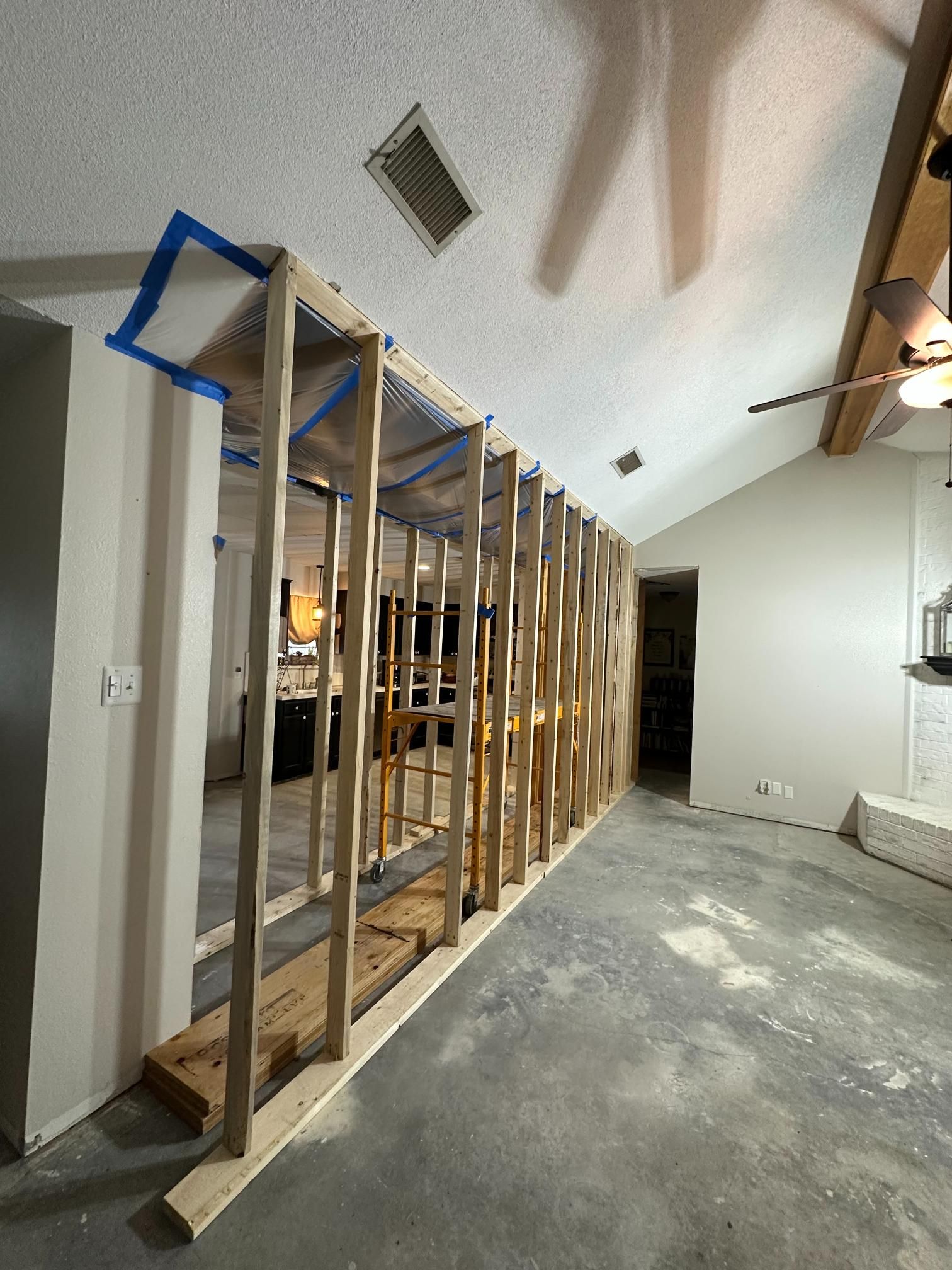 Interior view of a partially constructed wooden wall framing.  Blue tape is visible. Concrete floor.
