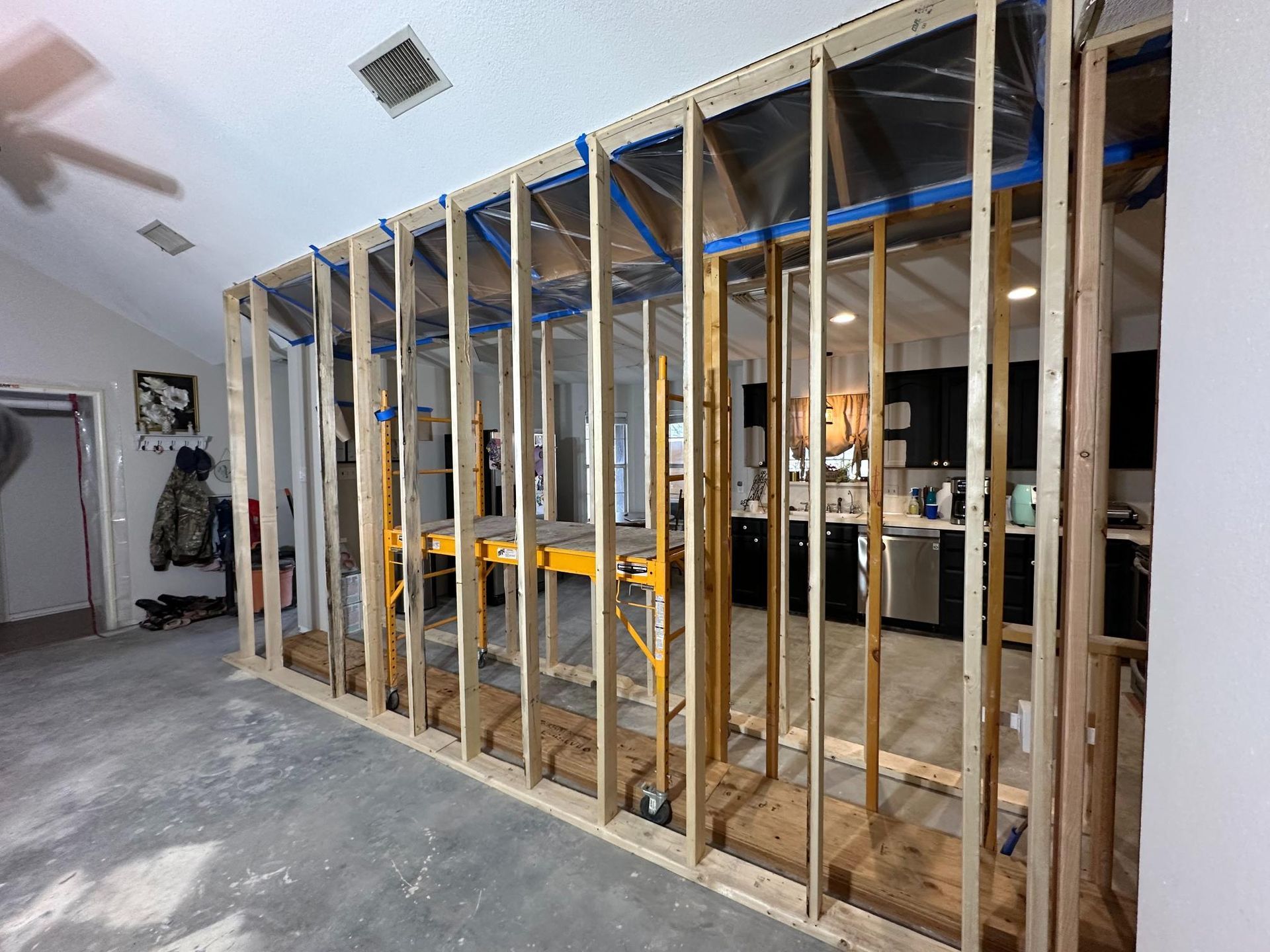 Interior with exposed wooden wall framing, open to a kitchen with dark cabinets and stainless steel appliances.