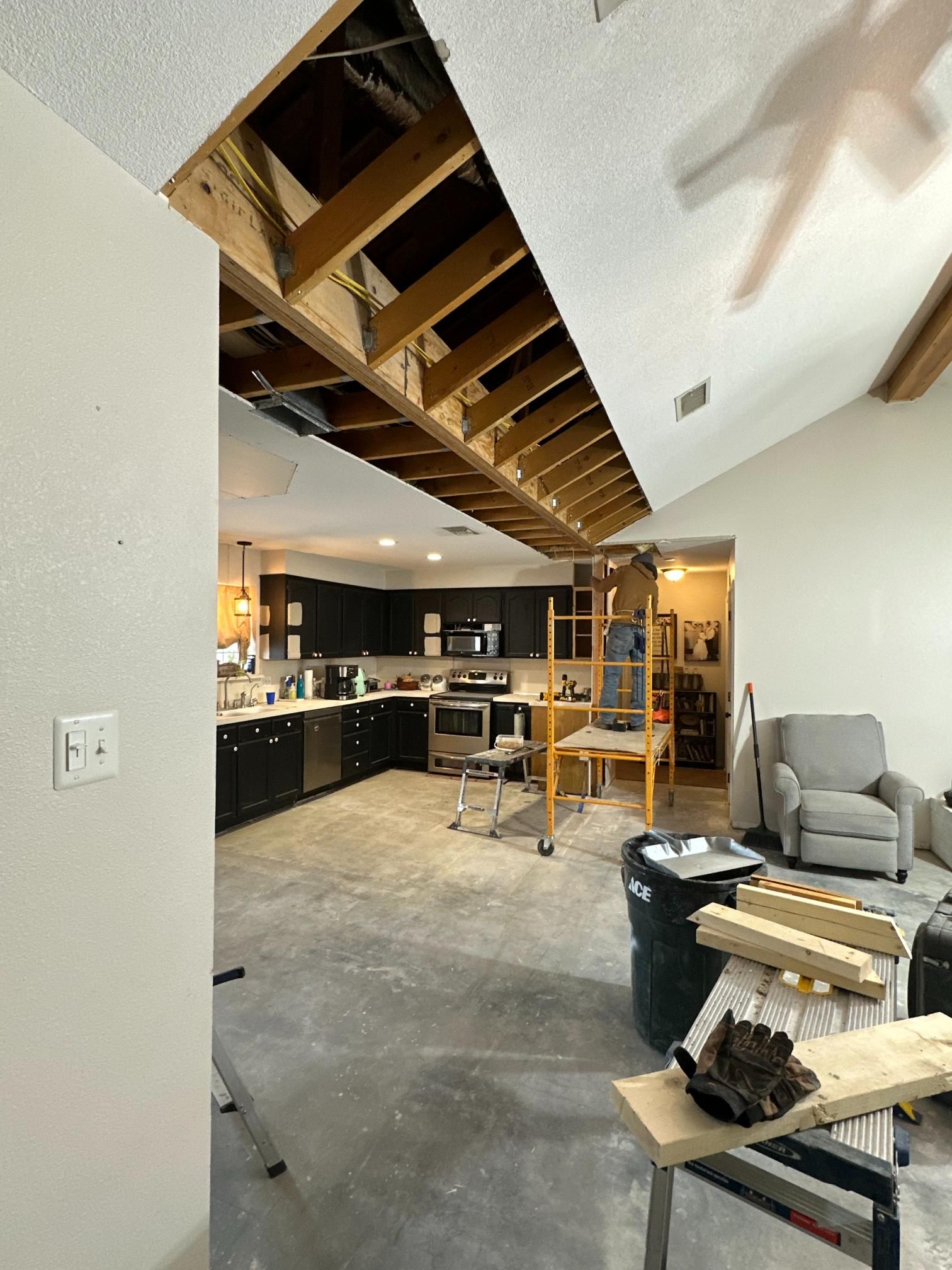 Kitchen and living room renovation. Exposed ceiling beams, ladder, cabinets, and debris.