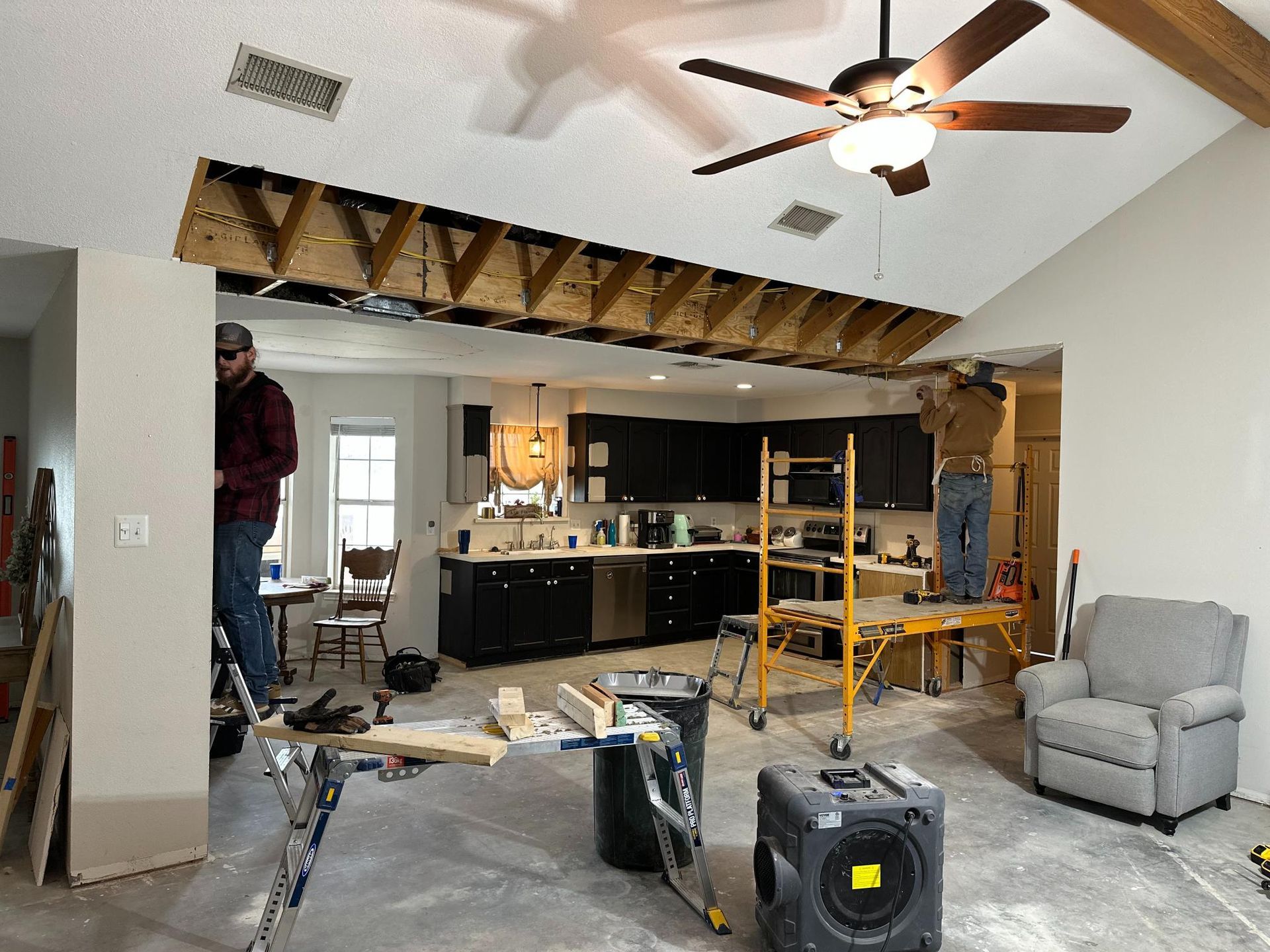 Men working on ceiling, removing drywall, exposing beams in kitchen. Construction scene.