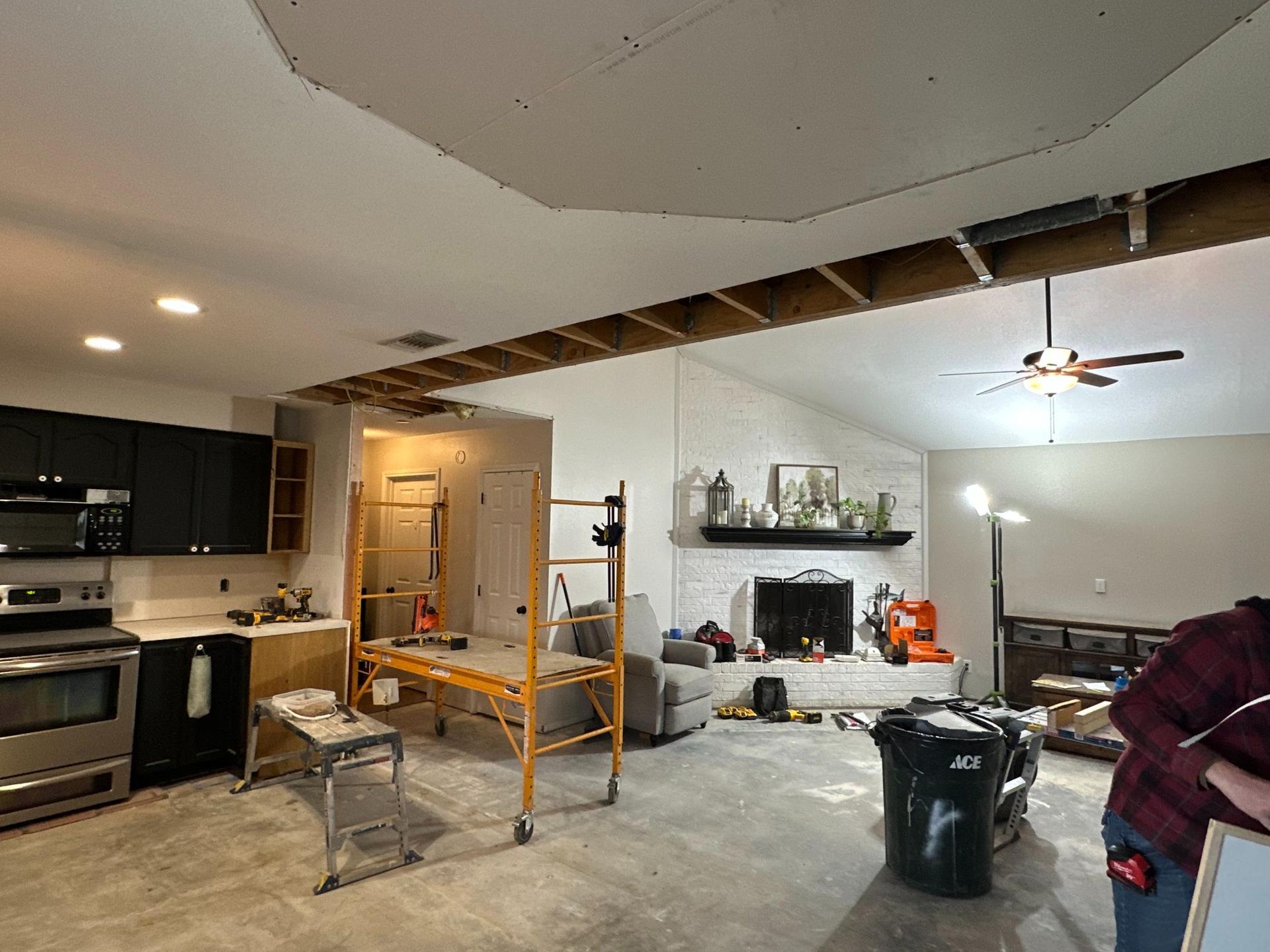 Interior view of a room under construction with exposed ceiling beams, a partially completed kitchen, and a fireplace.