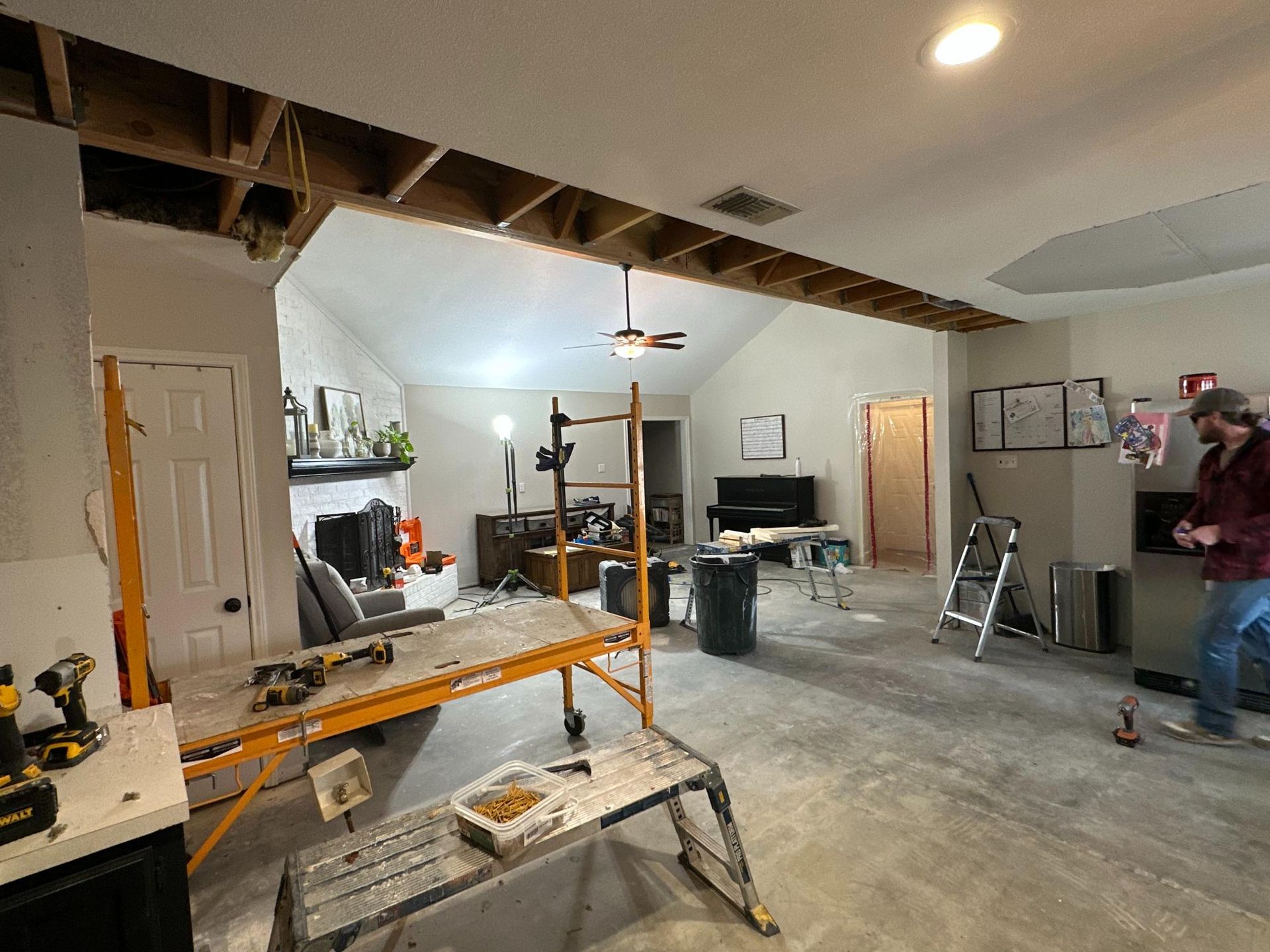 Interior undergoing renovation; open ceiling, scaffolding, tools, man working.