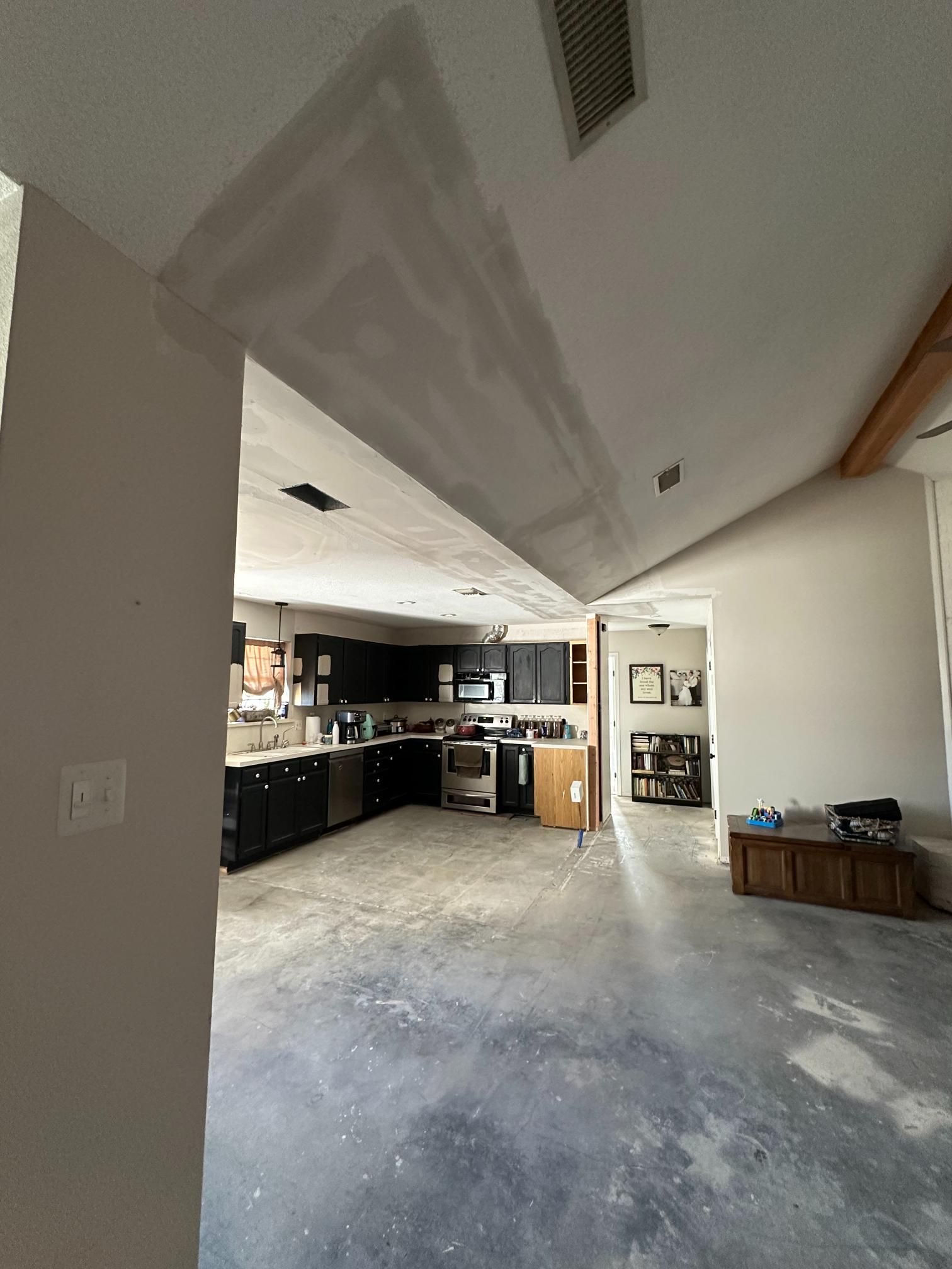 Interior shot of a home under renovation: kitchen, living area with exposed concrete floor, drywall, and a wooden beam.