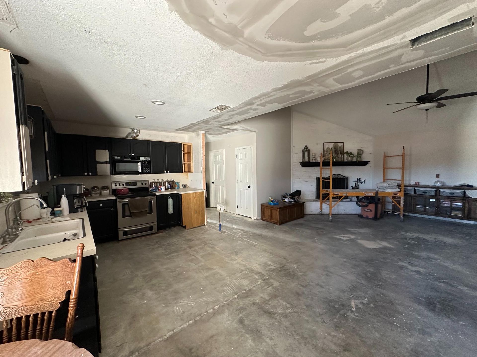 Kitchen undergoing renovation, with exposed ceiling, black cabinets, and open living area.