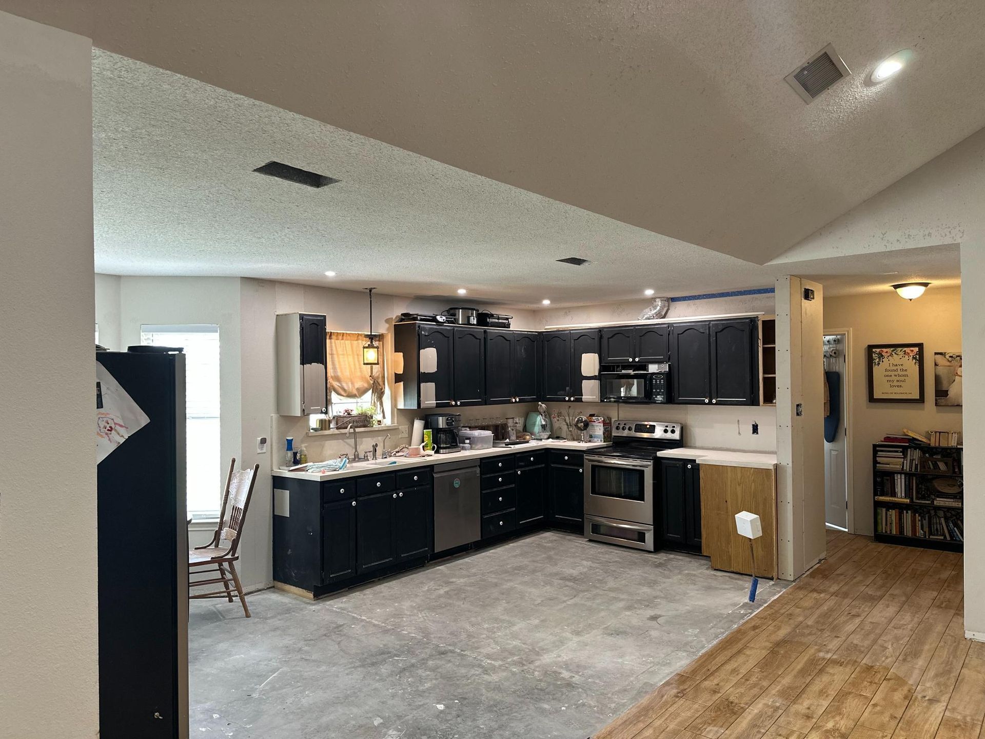 Kitchen with black cabinets, stainless steel appliances, and unfinished flooring.