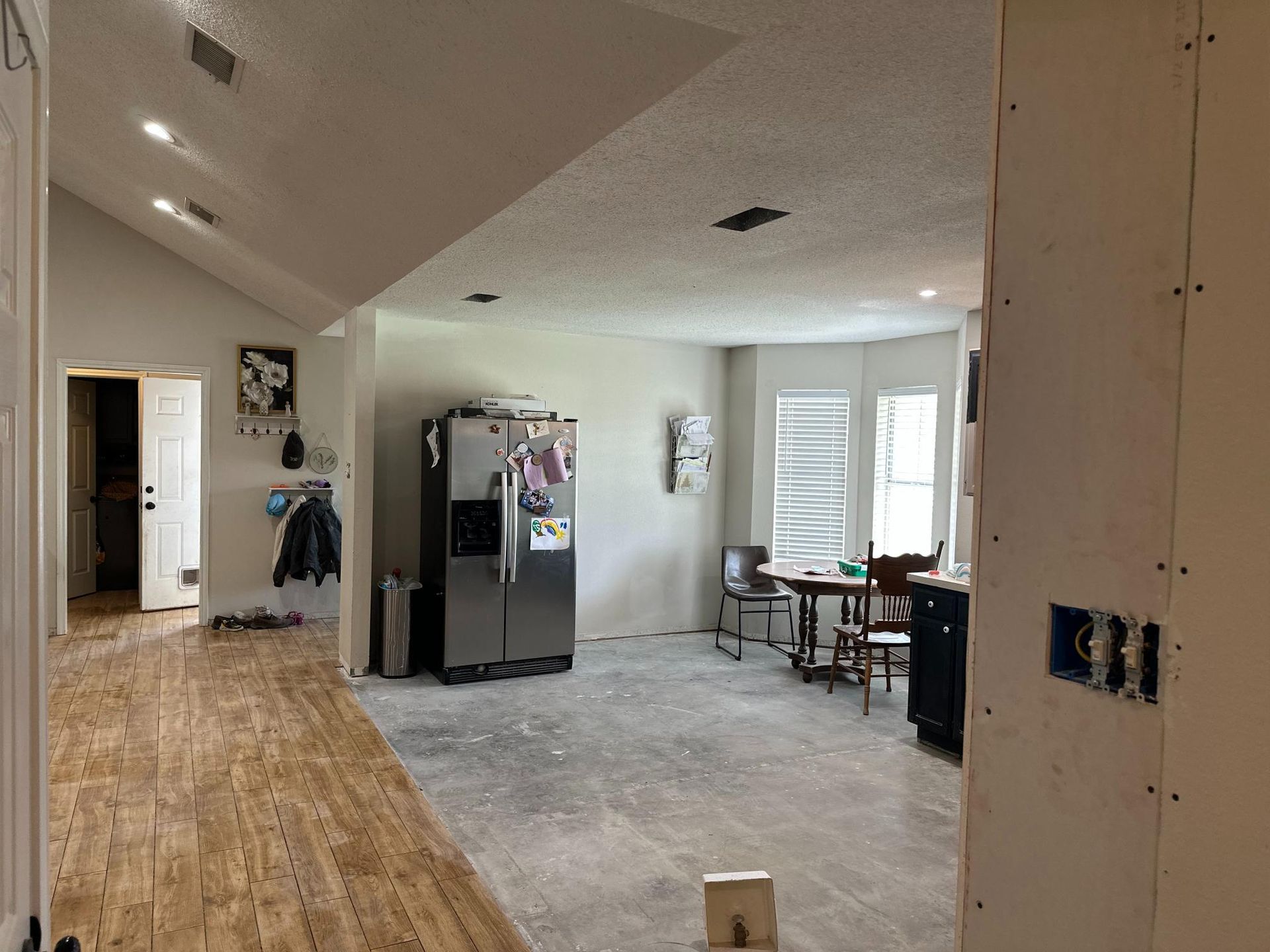 Kitchen under renovation, featuring a refrigerator, partially exposed drywall, and a dining table.