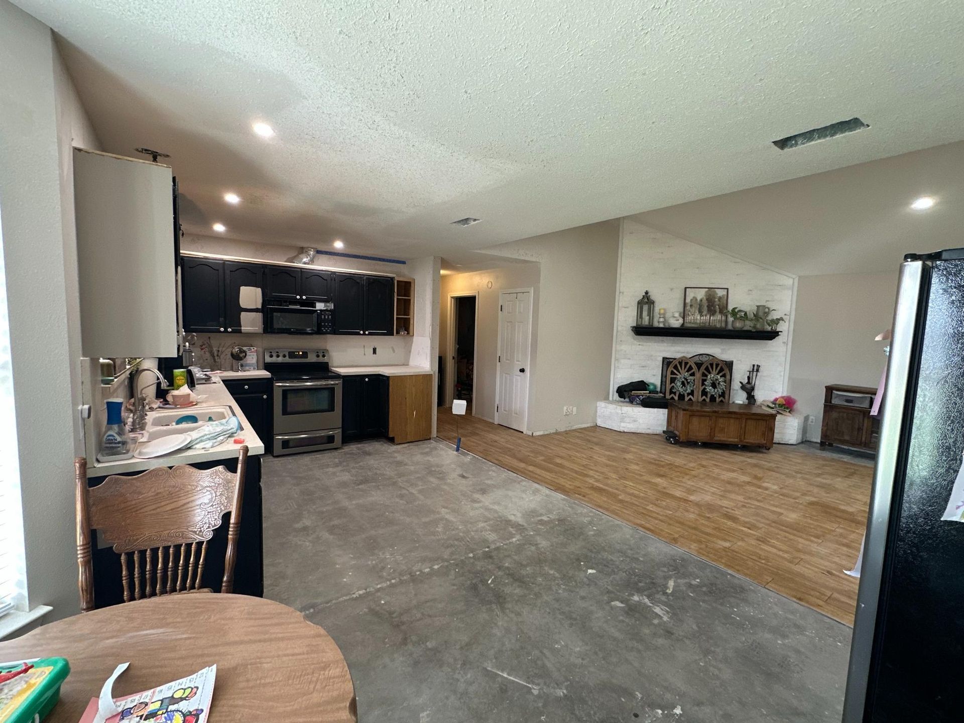 Kitchen under renovation with exposed concrete floor, black cabinets, white walls, and fireplace.