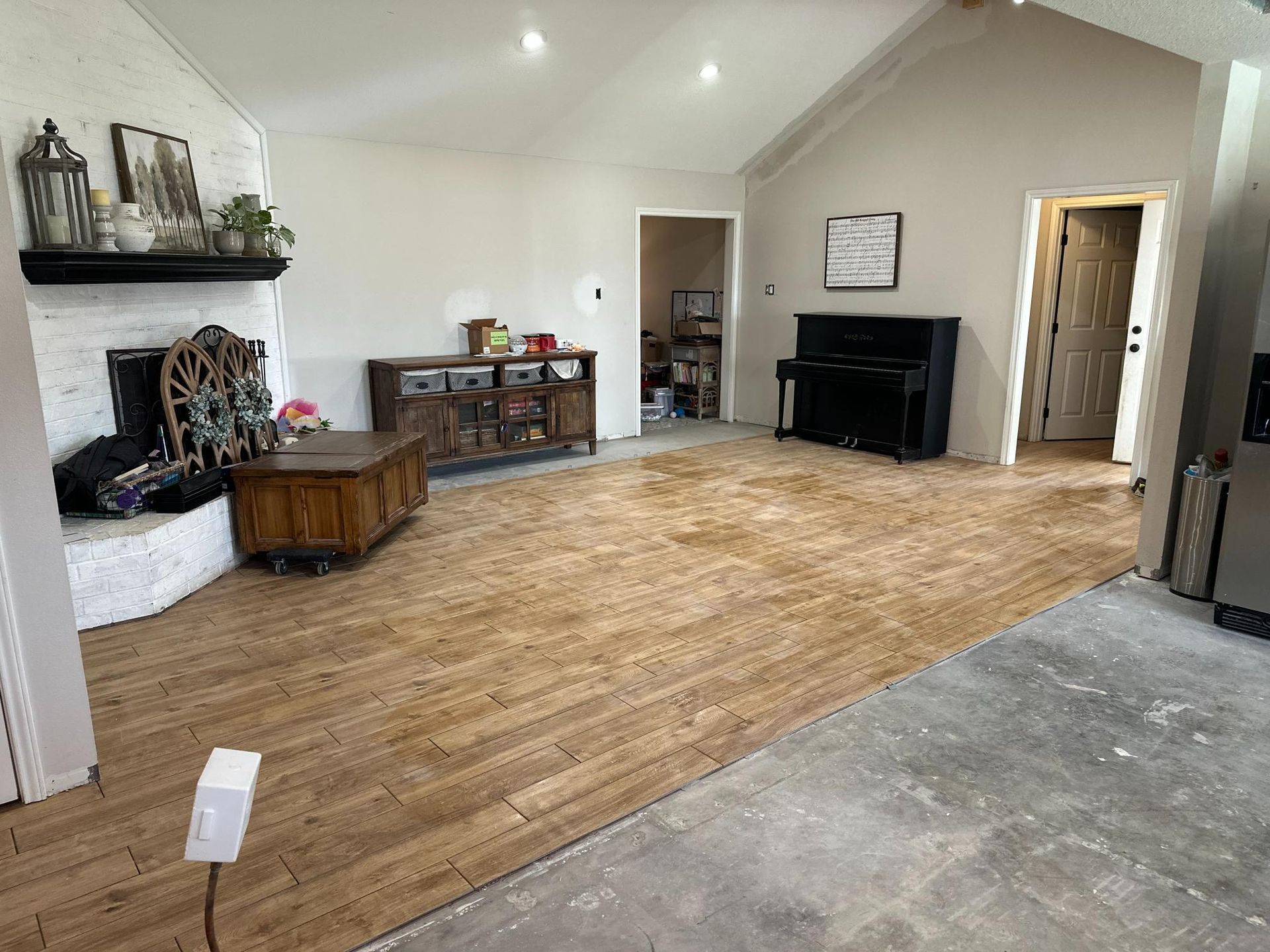 Living room with exposed wood floor, fireplace, and piano, awaiting renovation.