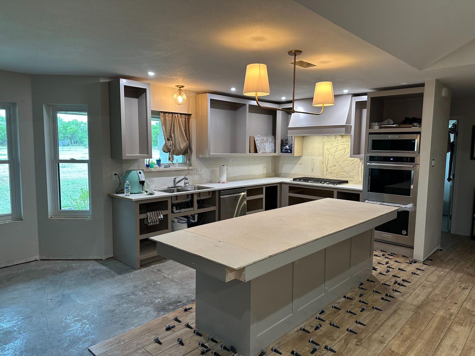 Kitchen remodel in progress: grey cabinets, island with countertop, exposed walls, unfinished flooring.