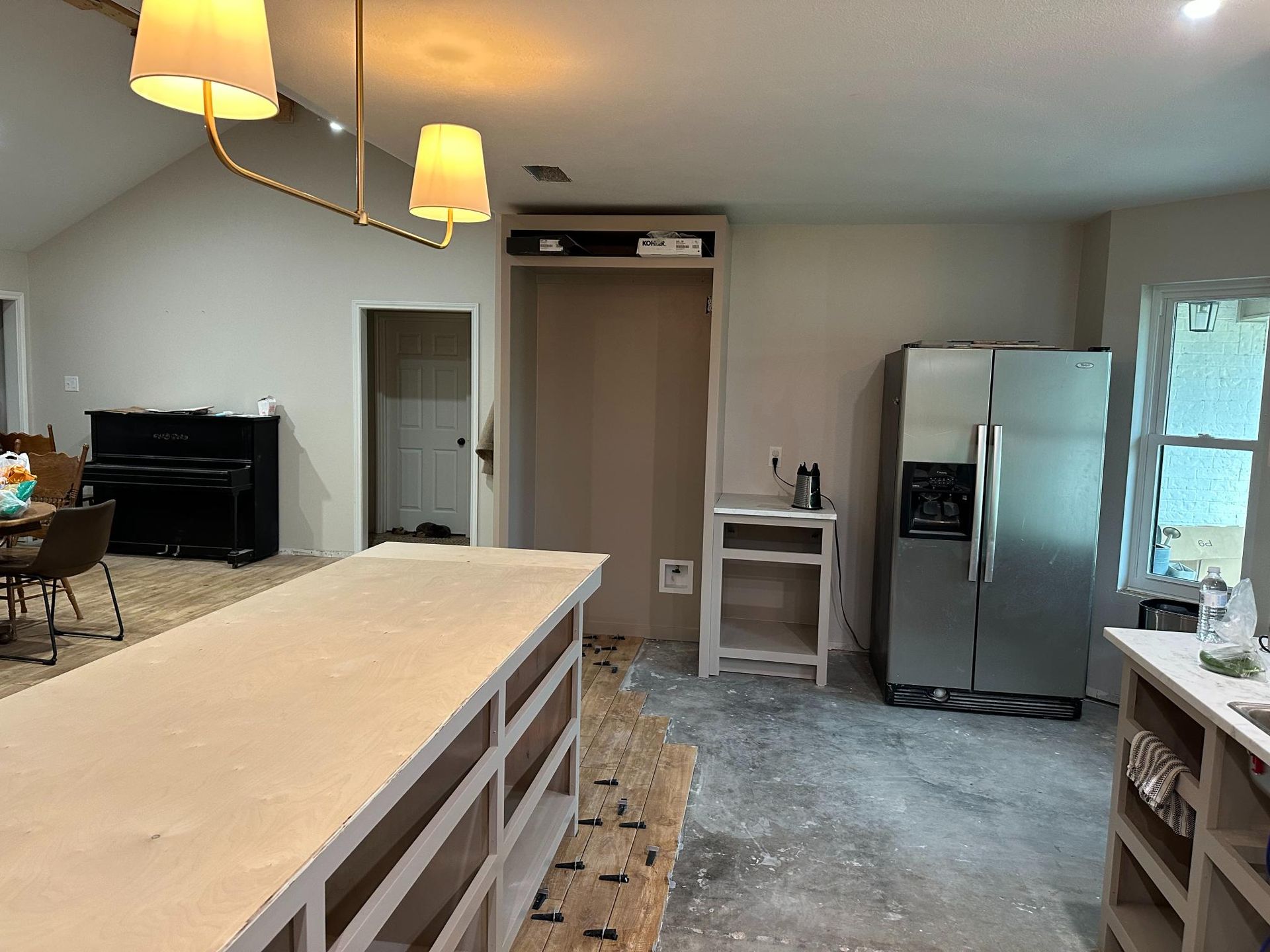 Kitchen under renovation; island, refrigerator, cabinets, lift, piano, and light fixture.
