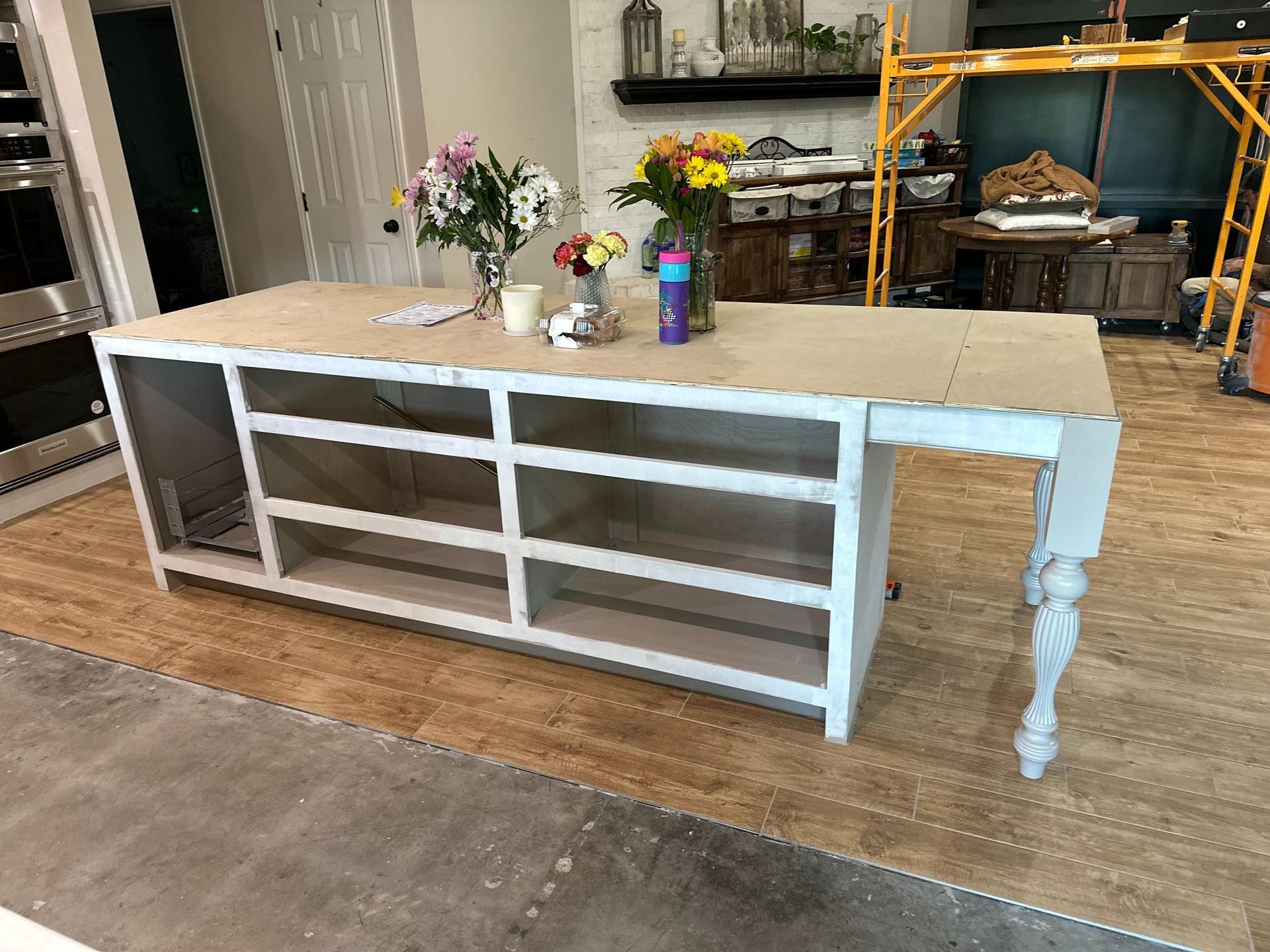 Partially constructed kitchen island with white cabinets, light countertop, and a decorative leg.