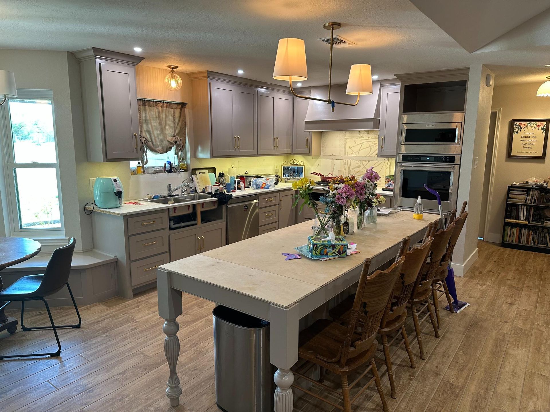 Kitchen with gray cabinets, large island, and wooden chairs; flowers and appliances are visible.