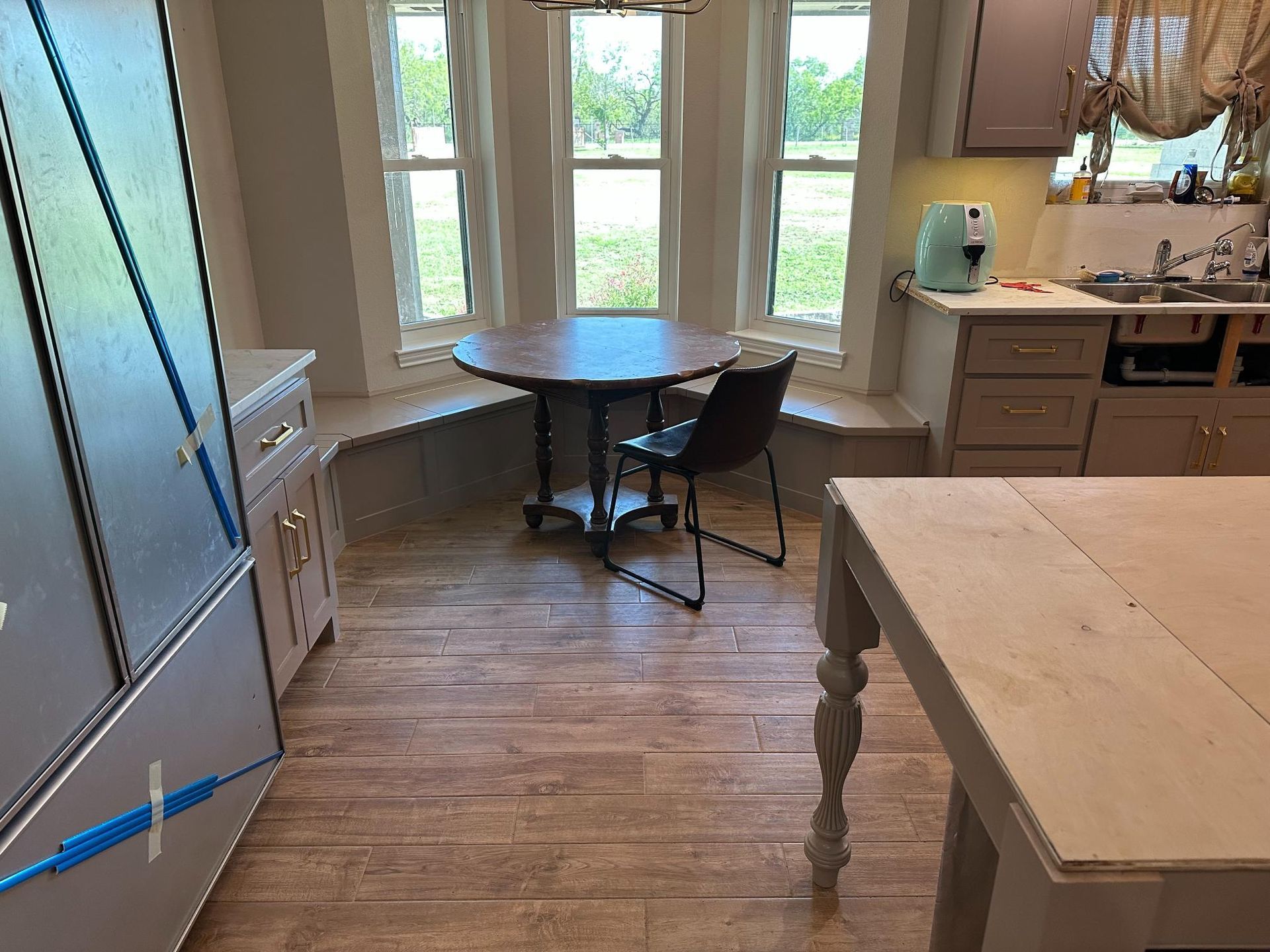 Kitchen with bay window, small table, single chair, and light-colored cabinets and flooring.