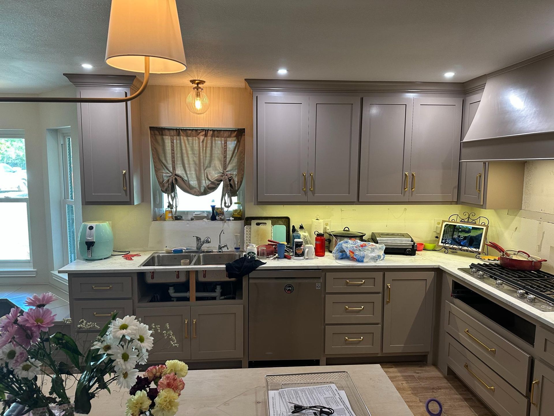 Kitchen with gray cabinets, stainless steel appliances, and a cooktop. Flowers and a lampshade are visible.