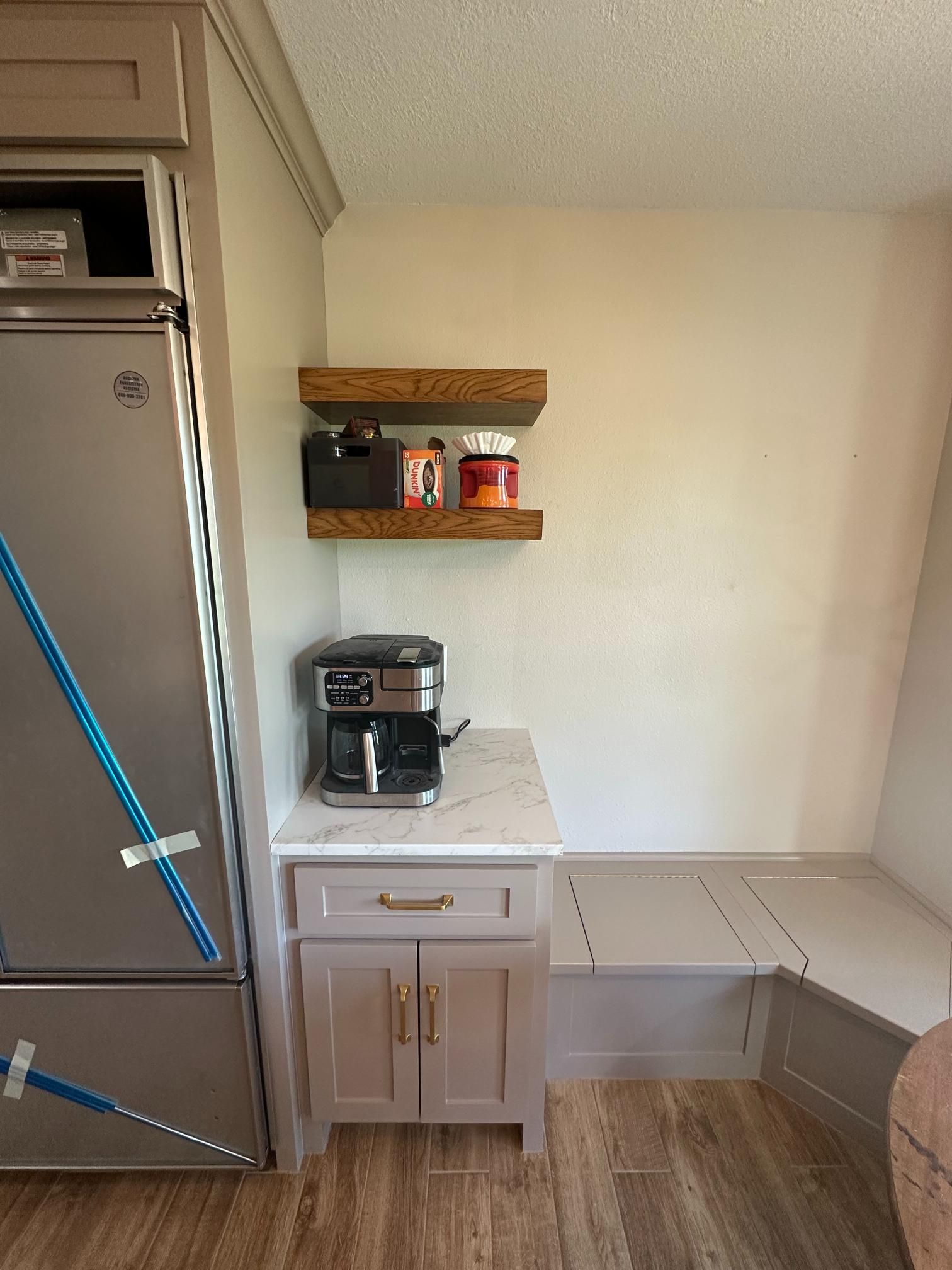 Coffee bar area: stainless steel fridge, beige cabinets, corner bench, floating shelves.