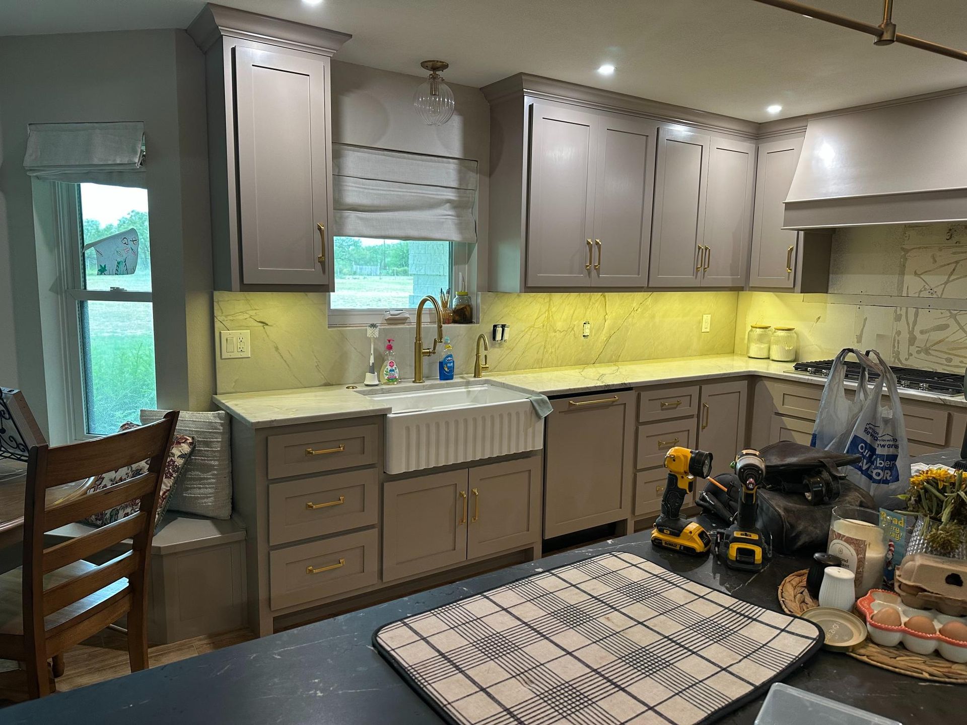 Kitchen with taupe cabinets, farm sink, under-cabinet lighting, window, and a black countertop.