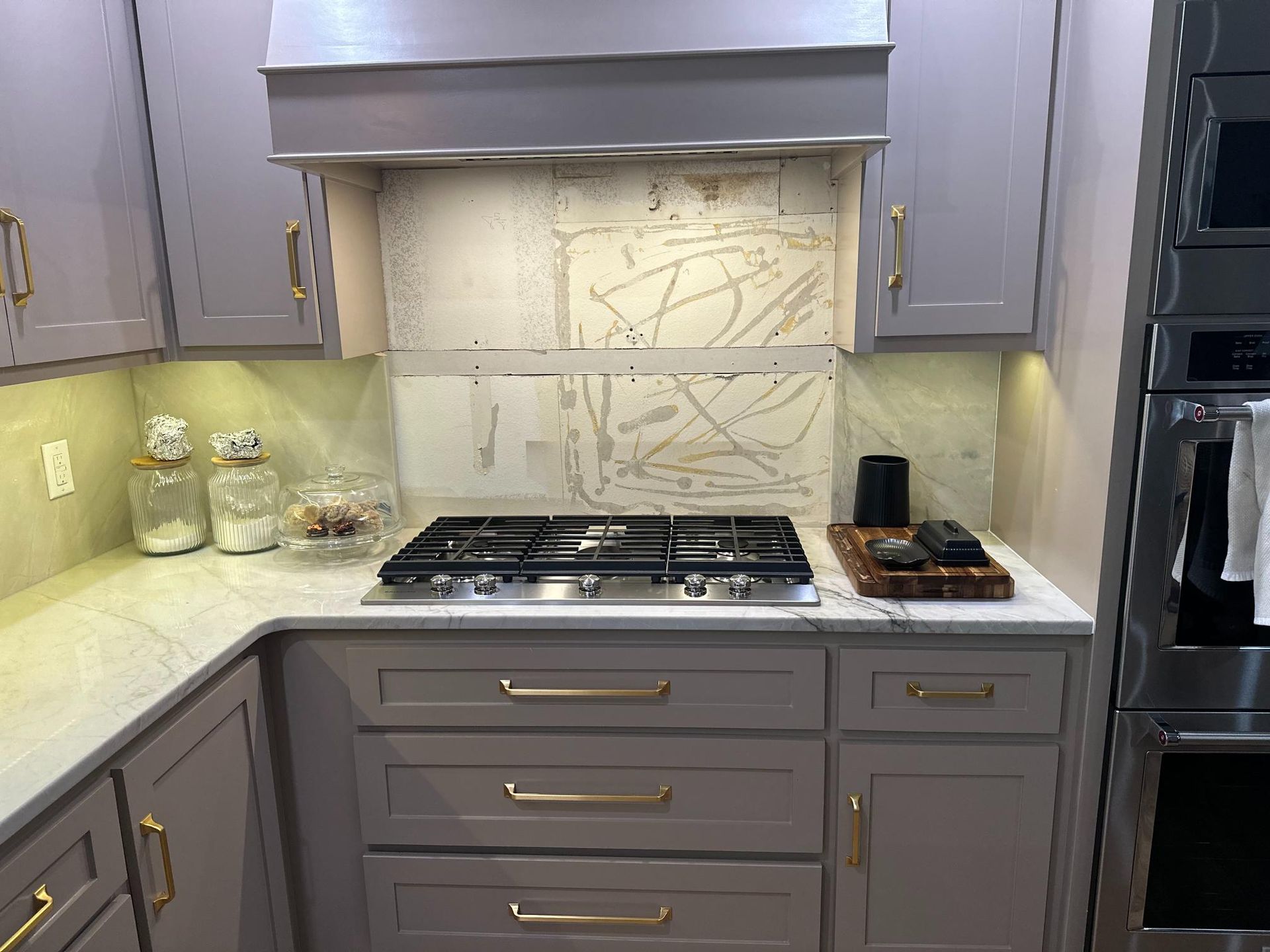 Kitchen with gray cabinets, gold hardware, gas stovetop, and unfinished backsplash.