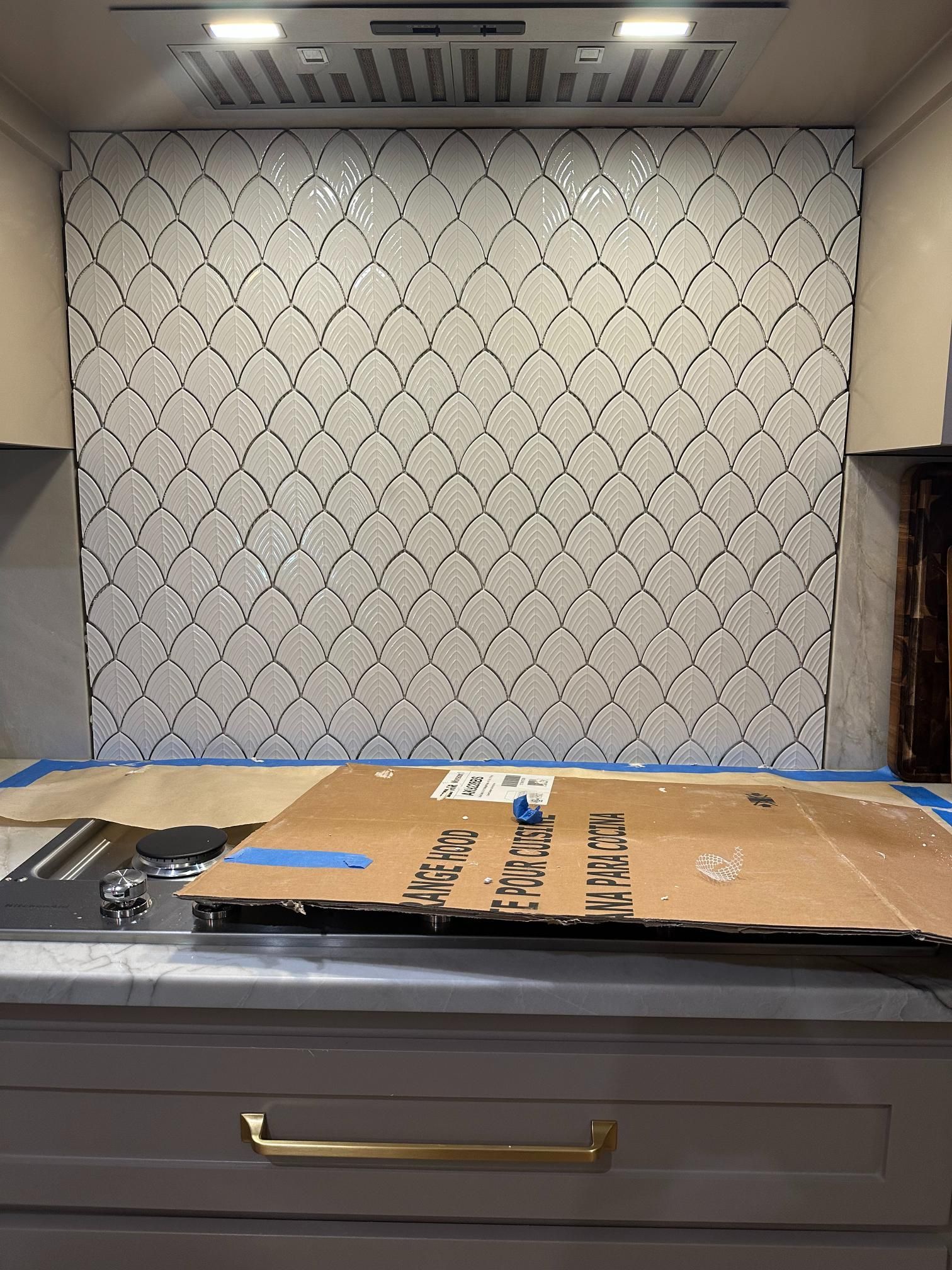 Kitchen backsplash installation with white patterned tiles and a ventilation hood.