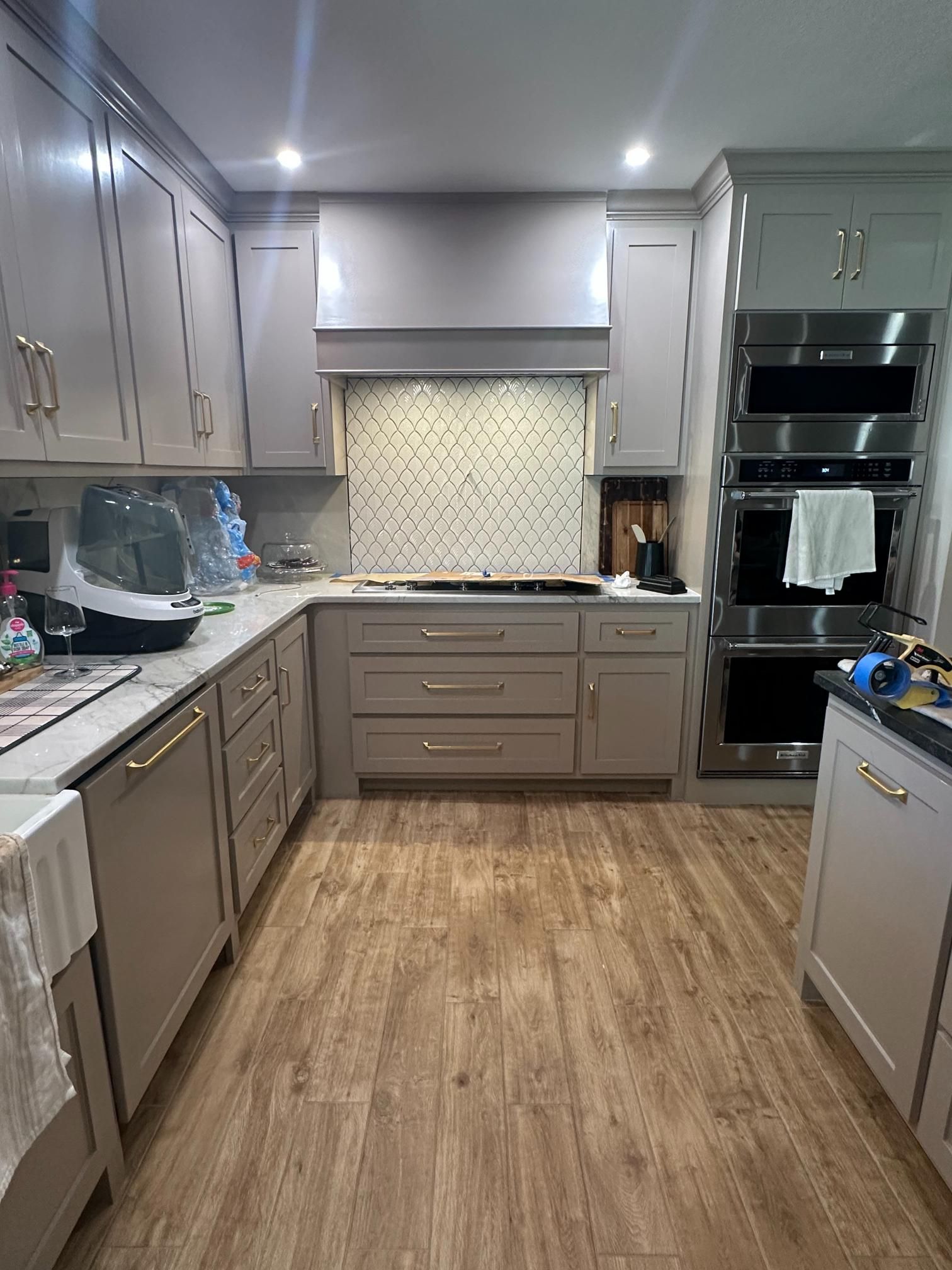 Modern kitchen with light gray cabinets, stainless steel appliances, and wood-look flooring.